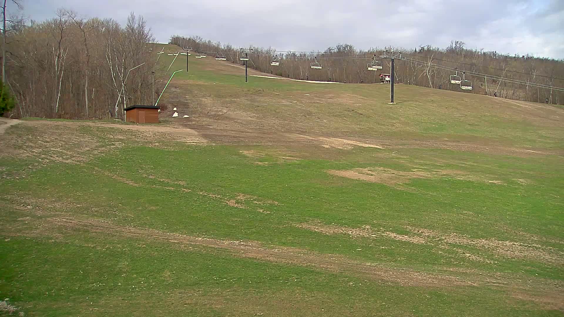 A grassy ski slope with a chairlift and a small brown building is visible under a cloudy sky.
