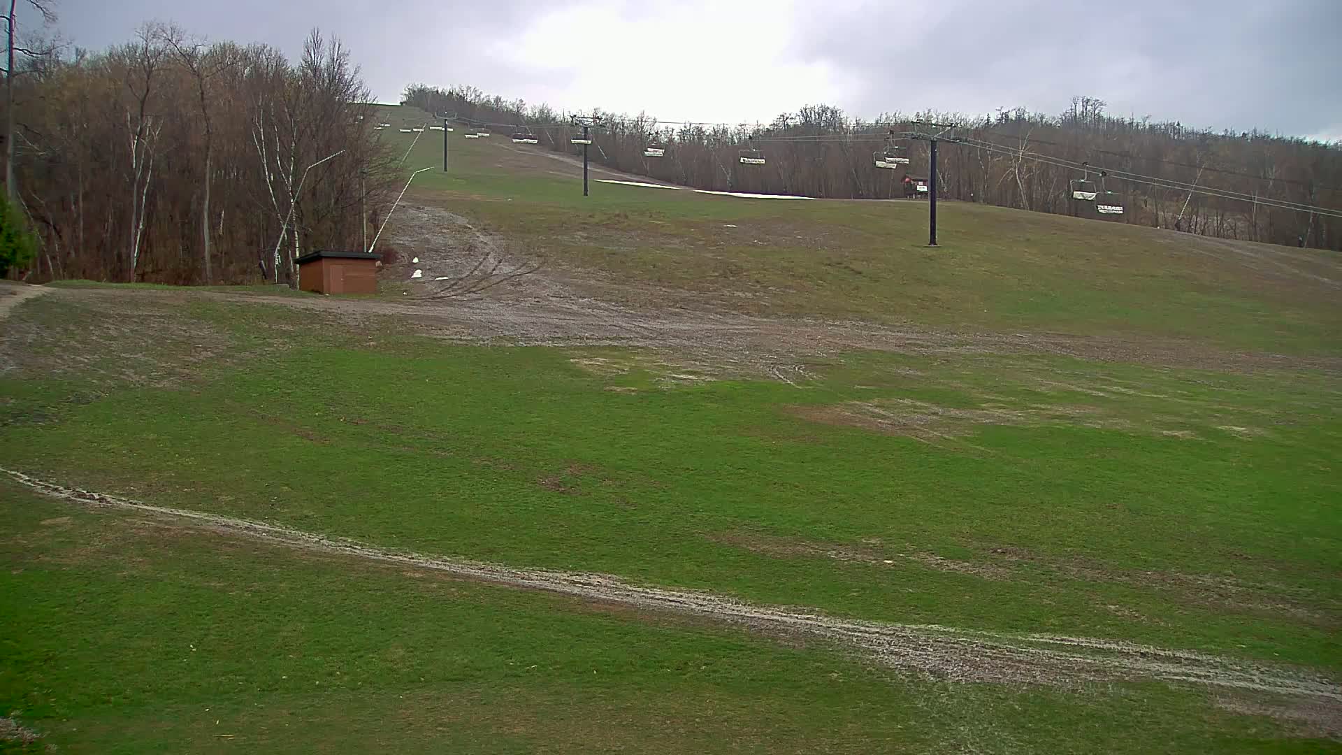 A grassy ski slope with an empty chairlift and a small building under an overcast sky.