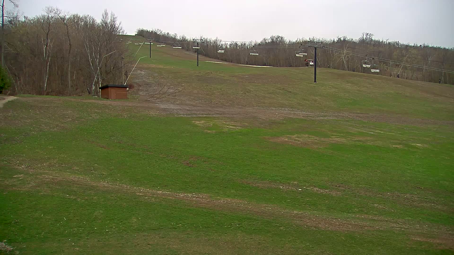 A grassy hill with a ski lift and a small brown building is visible under an overcast sky.
