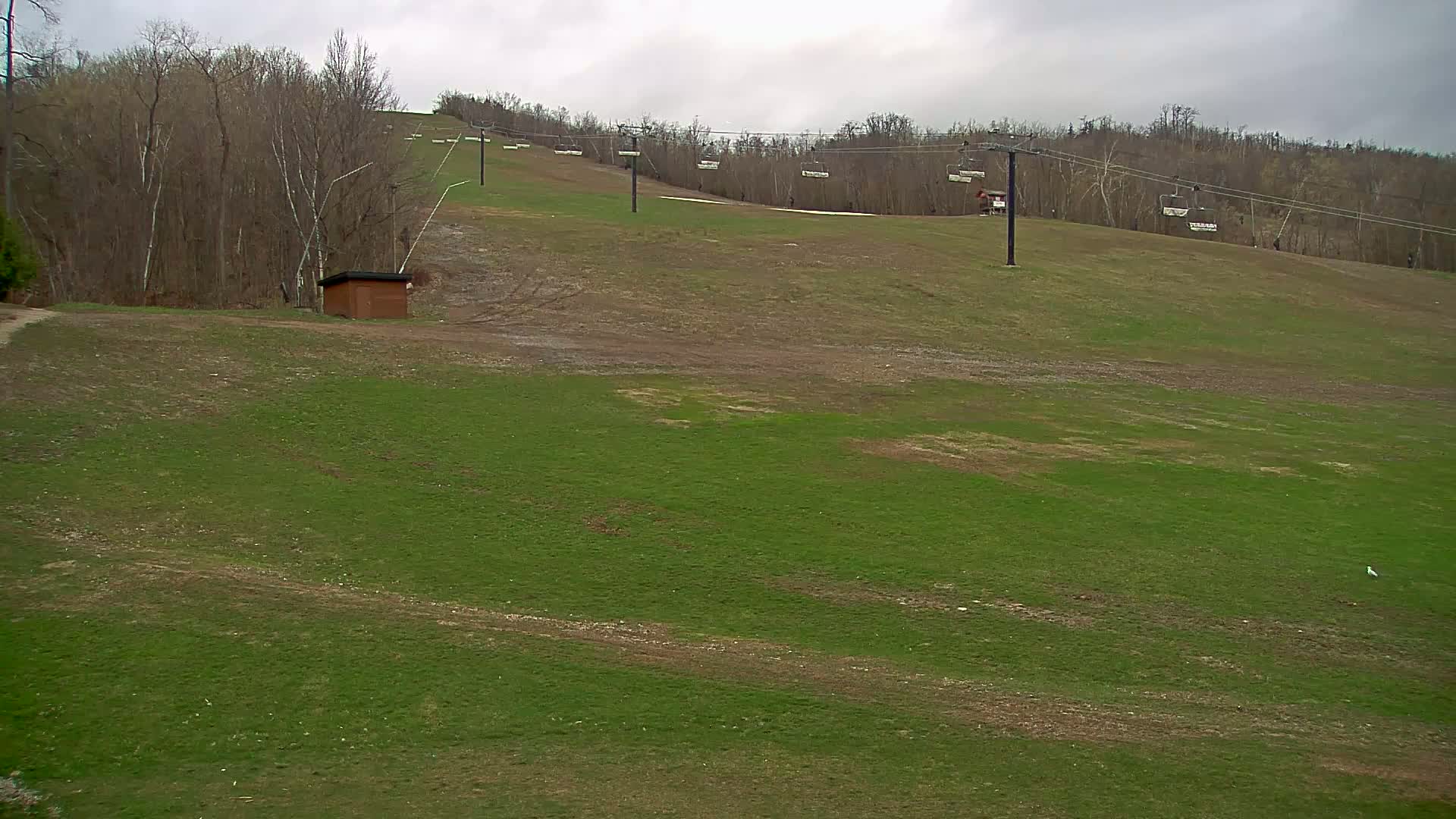 A grassy ski slope with a chairlift and a small building is visible under an overcast sky.