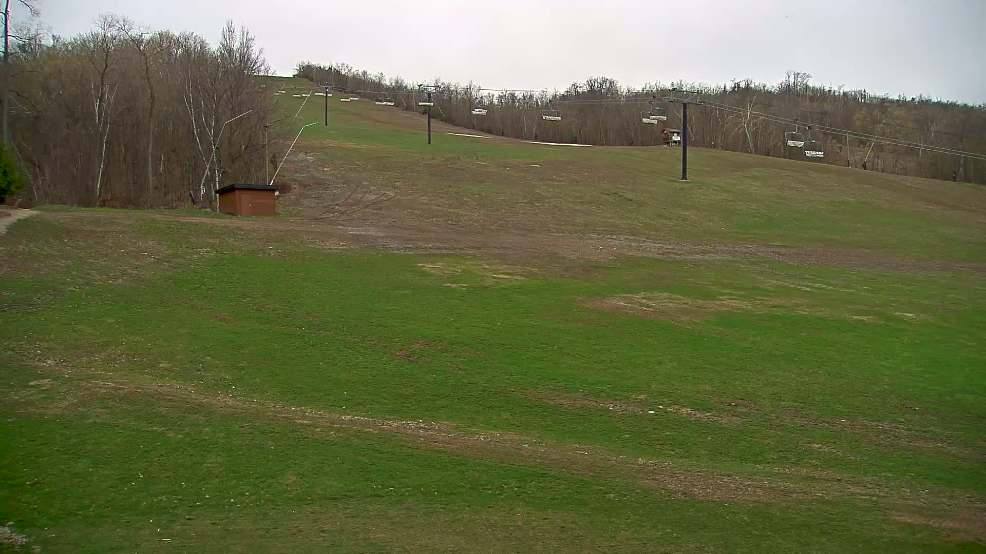 A grassy ski slope with a chairlift and a small building is visible under an overcast sky.