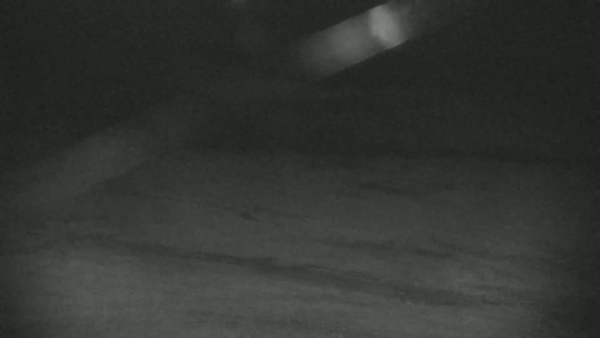 A dark, blurry image shows a dimly lit, possibly outdoor, area at night with a bright light source in the upper right corner.