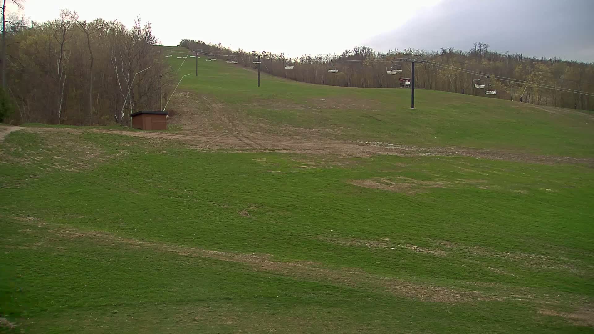 A grassy hillside with a ski lift and a small brown building under an overcast sky.