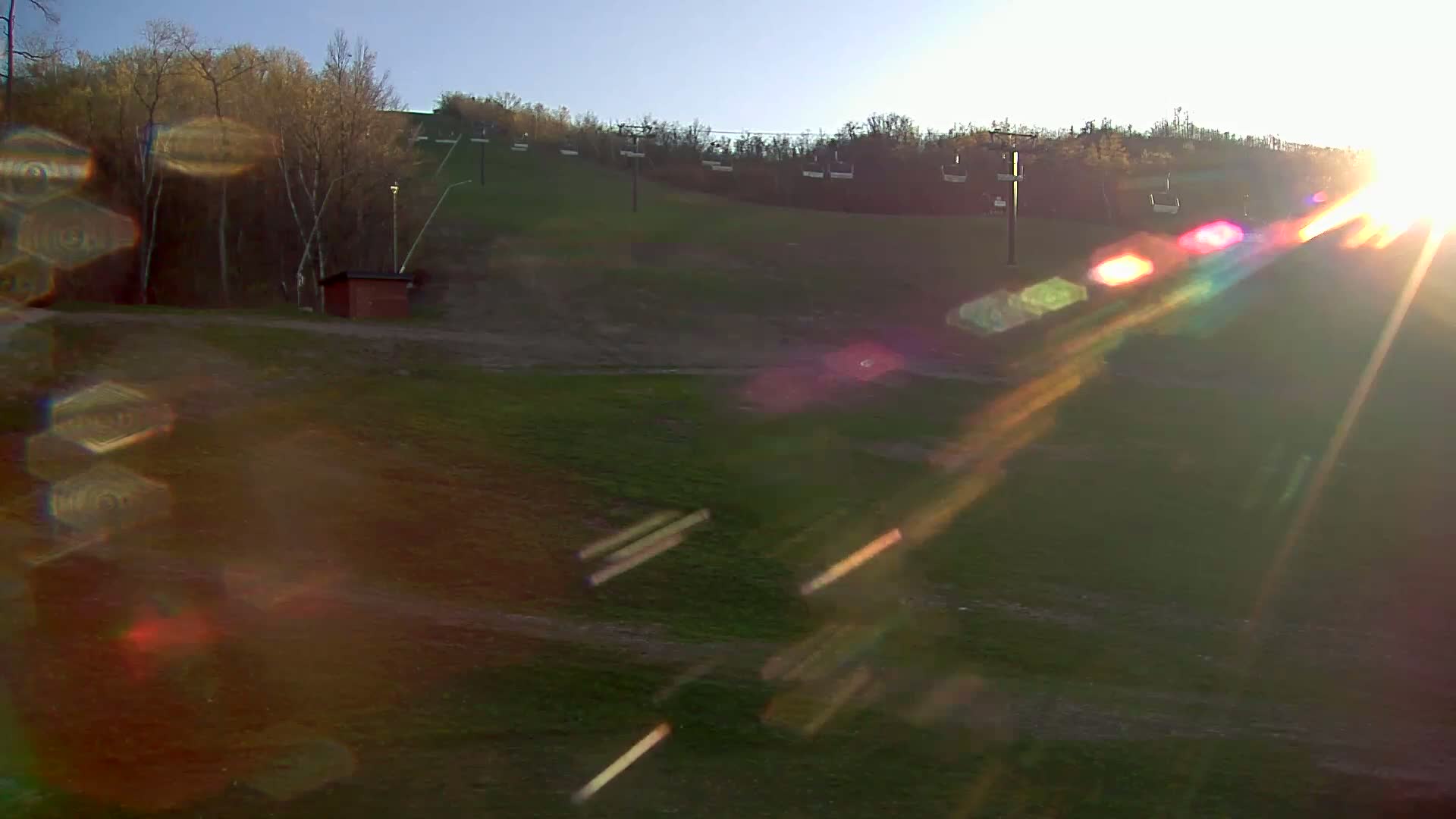 A grassy ski slope with chairlifts is bathed in bright sunlight on a clear day.