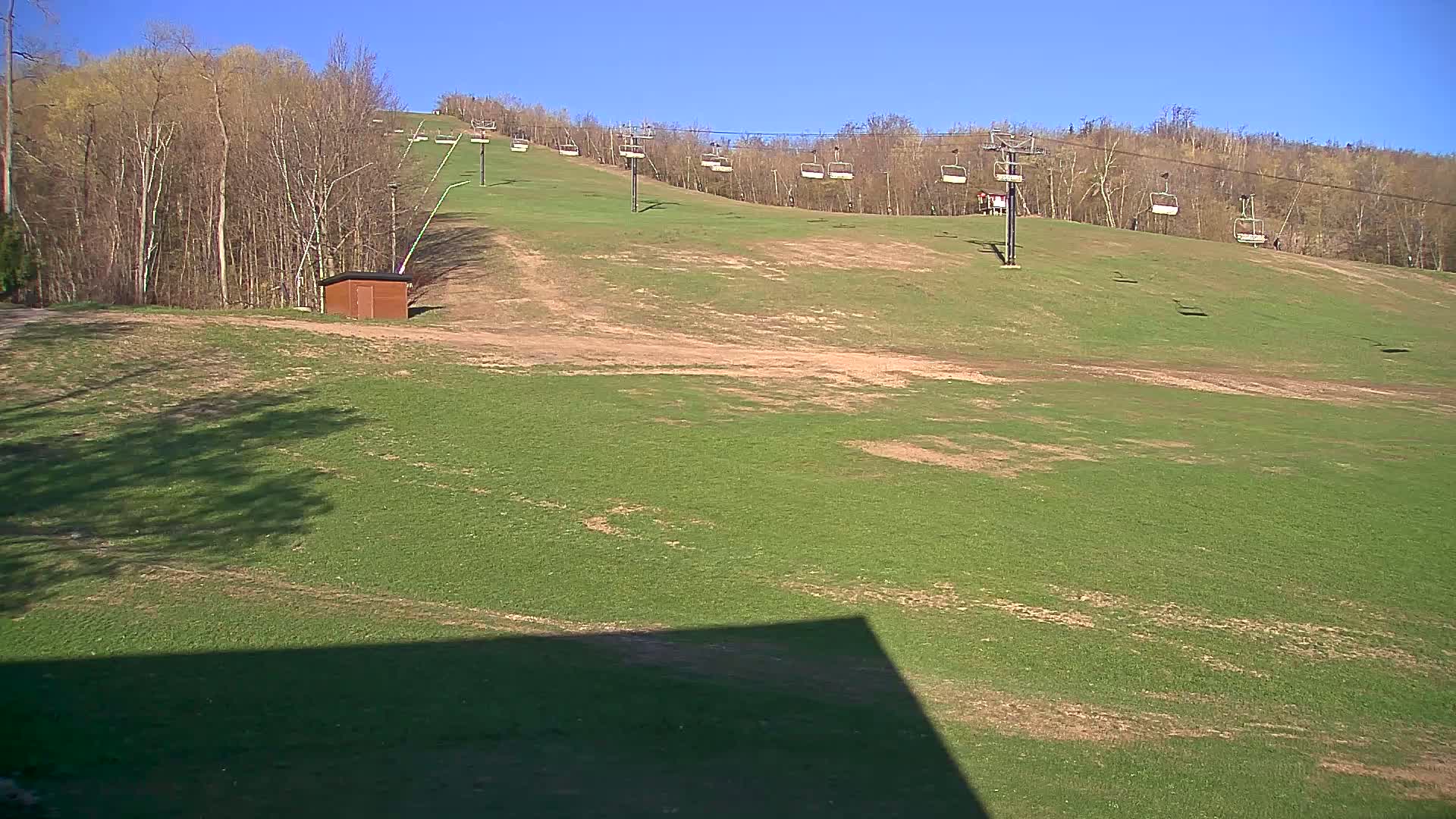 A grassy ski slope with a chairlift and a small shed is visible under a clear blue sky.