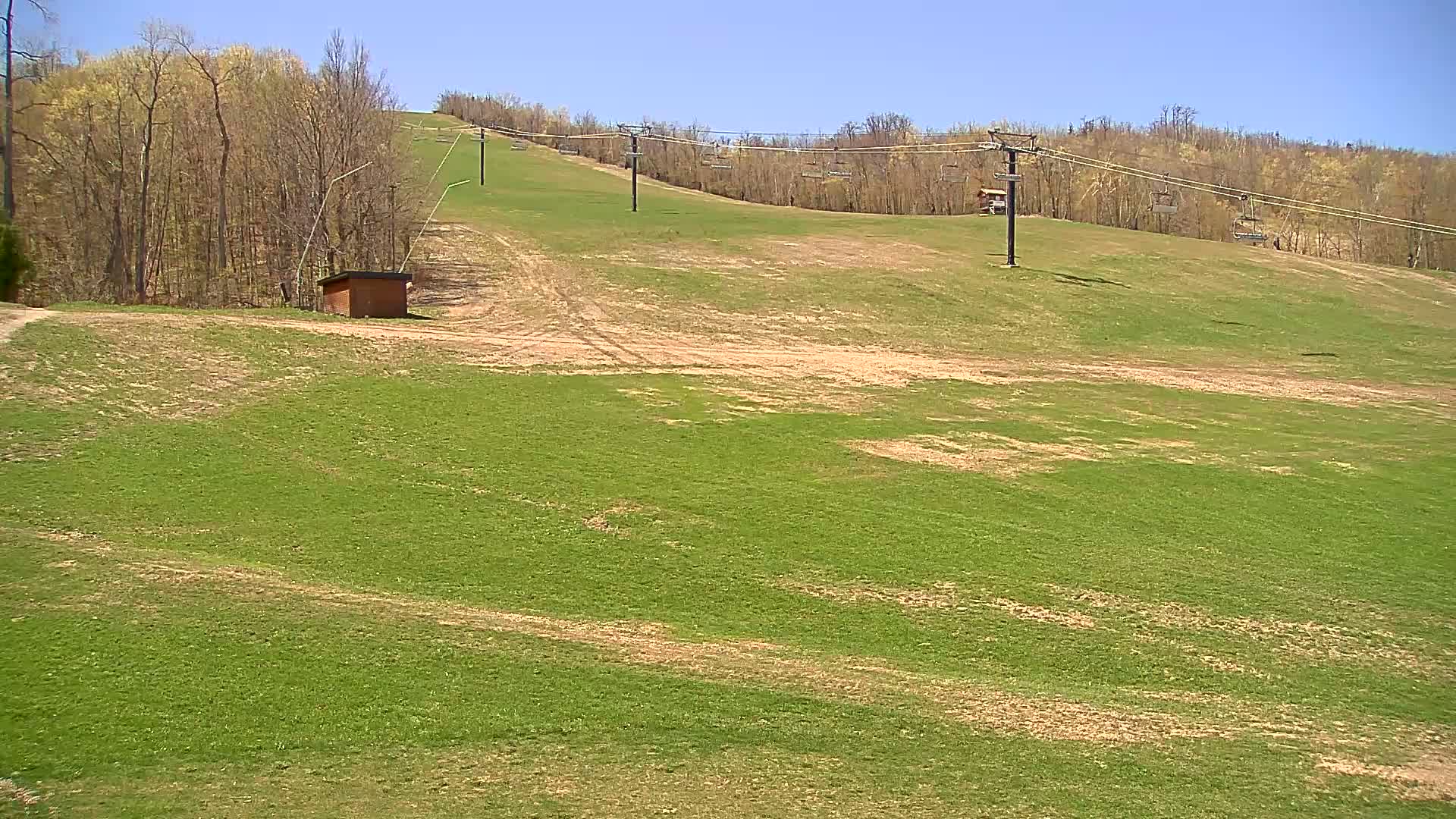 A grassy hillside with a chairlift and a small building, under a clear blue sky.