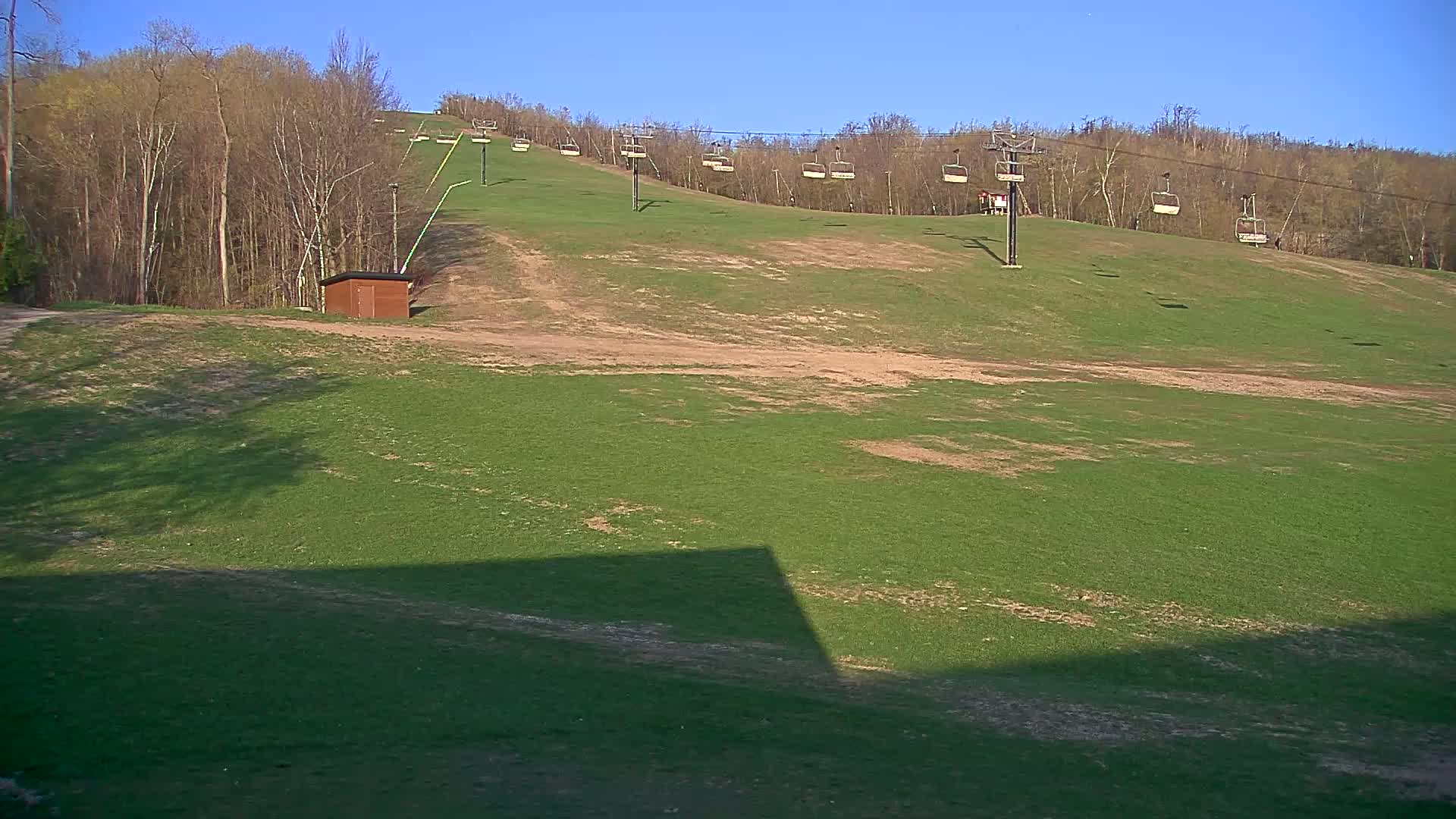 A grassy ski slope with a chairlift and a small building is visible under a clear blue sky.