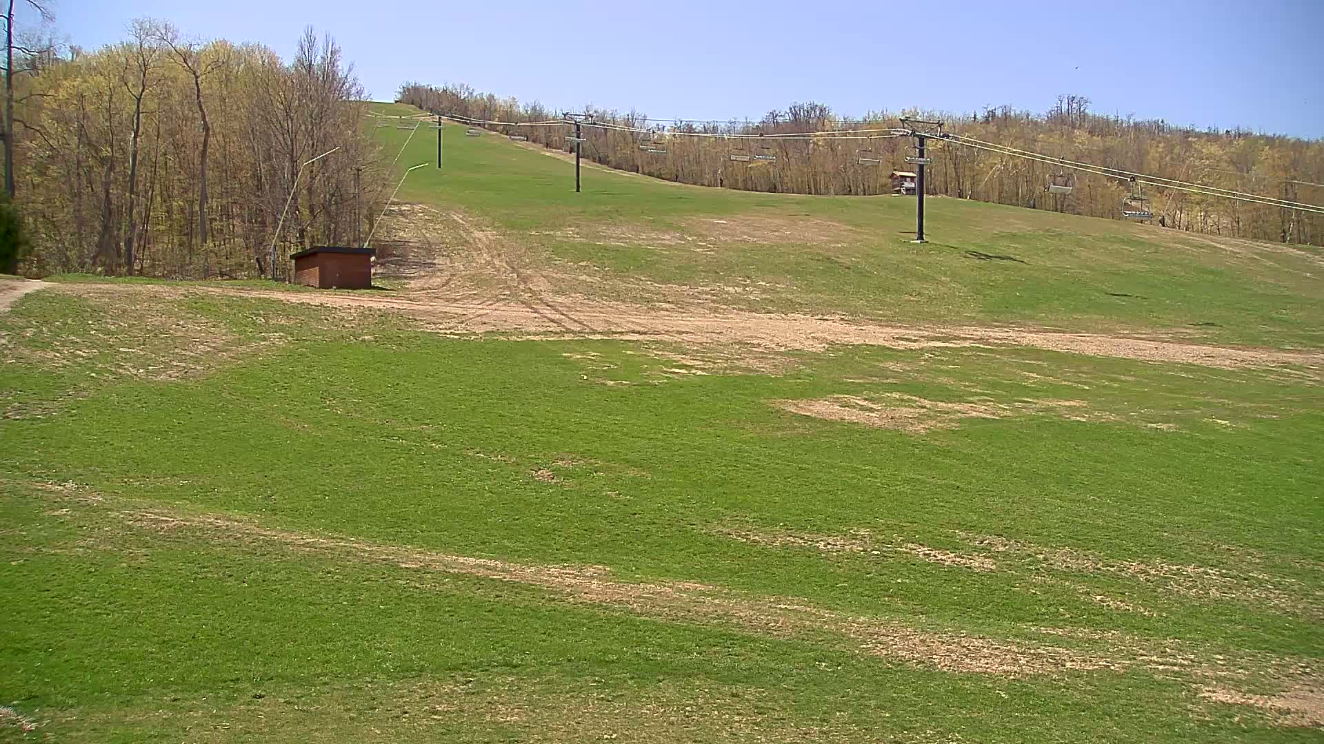 A grassy hillside with a chairlift and a small brown building is visible under a clear blue sky.