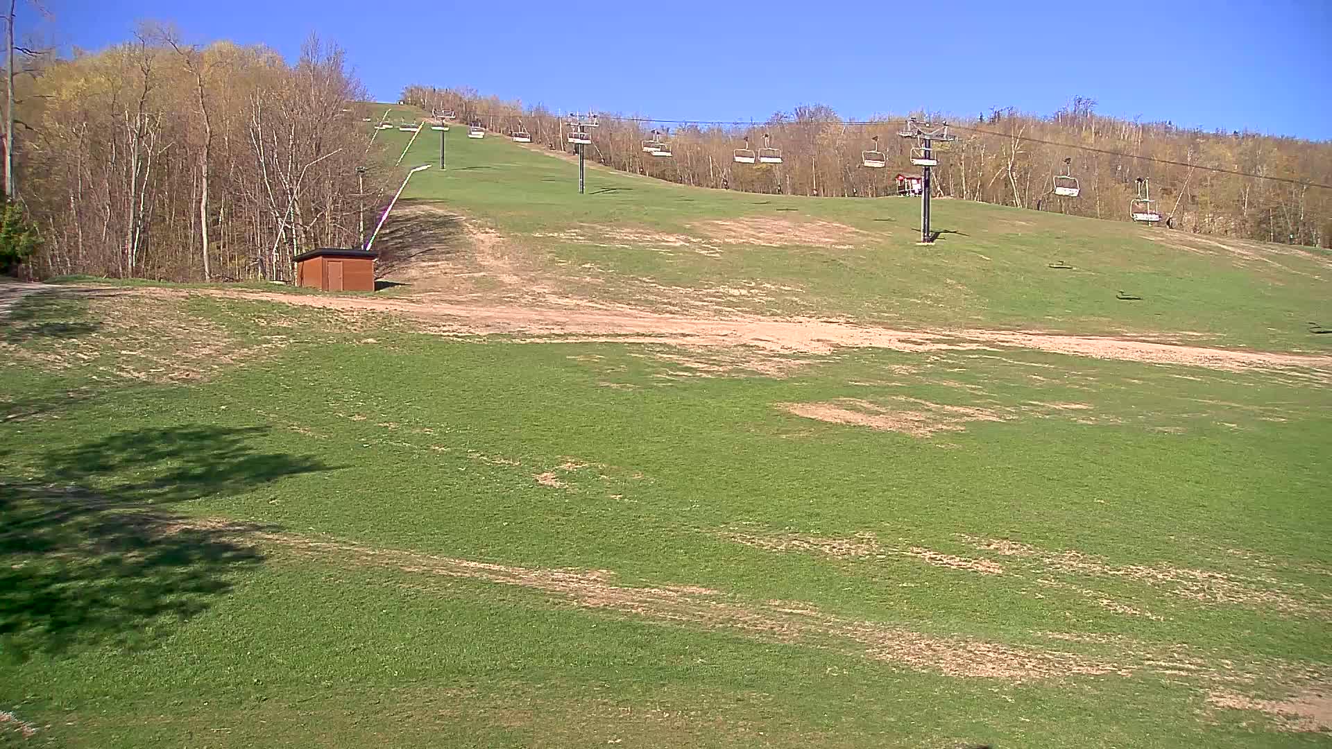 A grassy ski slope with a chairlift and a small building is visible under a clear blue sky.