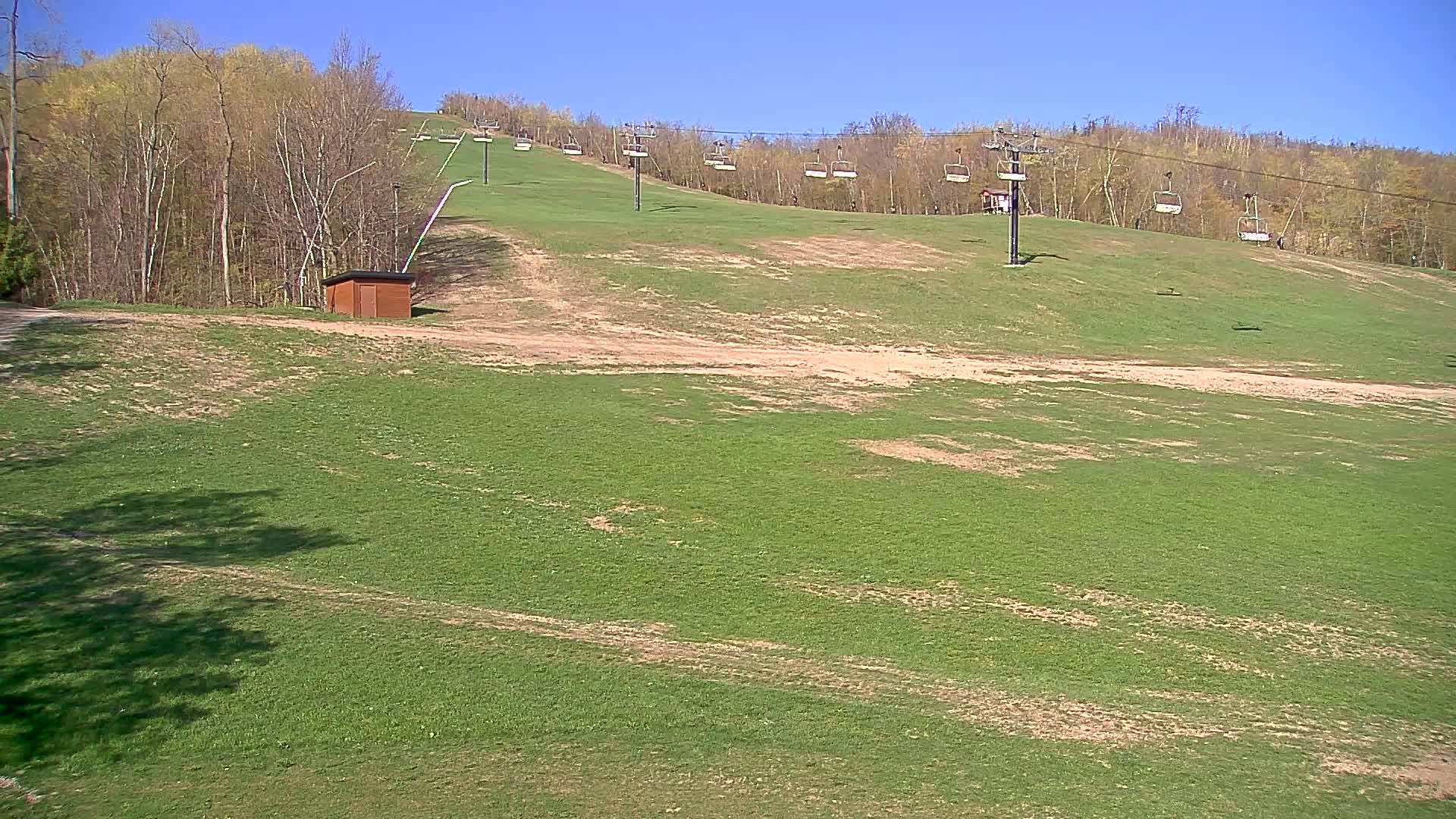 A grassy ski slope with a chairlift and a small building is visible under a clear blue sky.