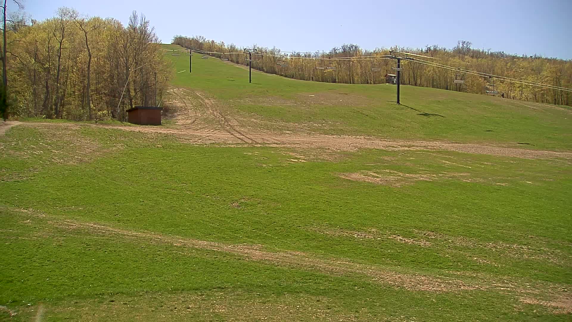 A grassy hillside with a ski lift and a small building is visible under a clear blue sky.
