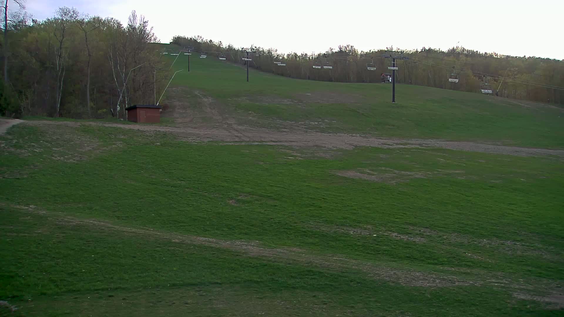 A grassy hill with a ski lift and a small building is visible under a cloudy sky.