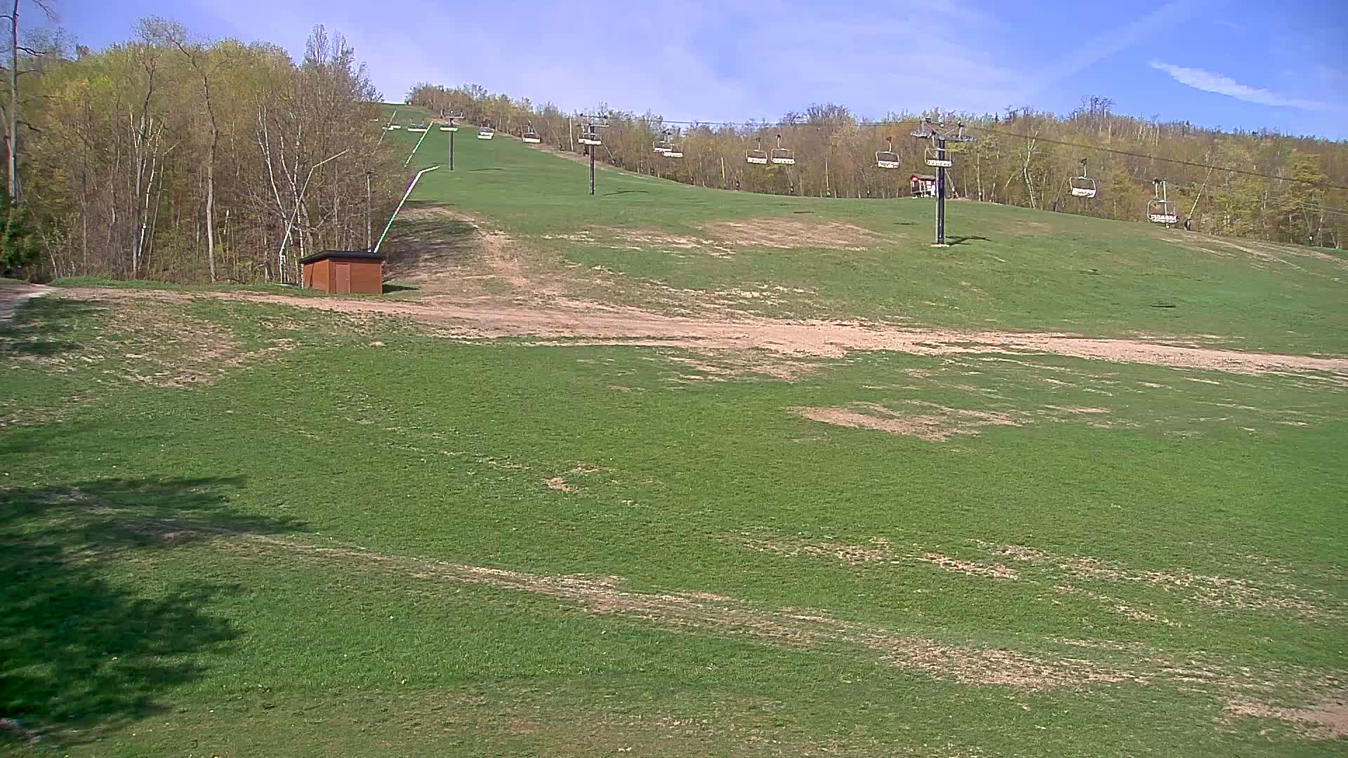 A grassy ski slope with a chairlift and a small building is visible under a sunny sky.