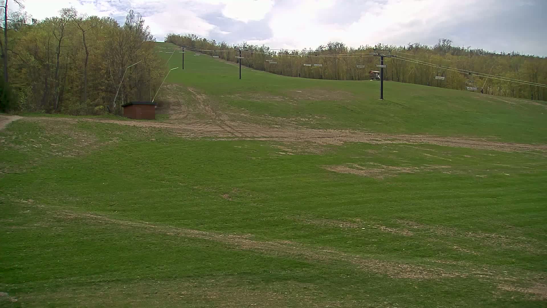 A grassy hill with a ski lift and a small brown building under a partly cloudy sky.