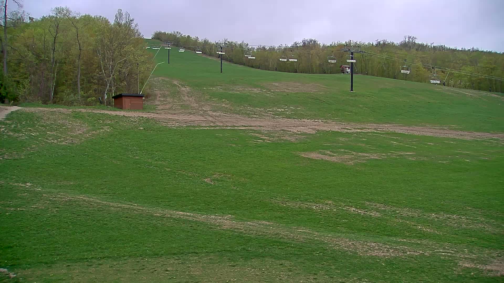 A grassy hill with a chairlift and a small brown building under an overcast sky.