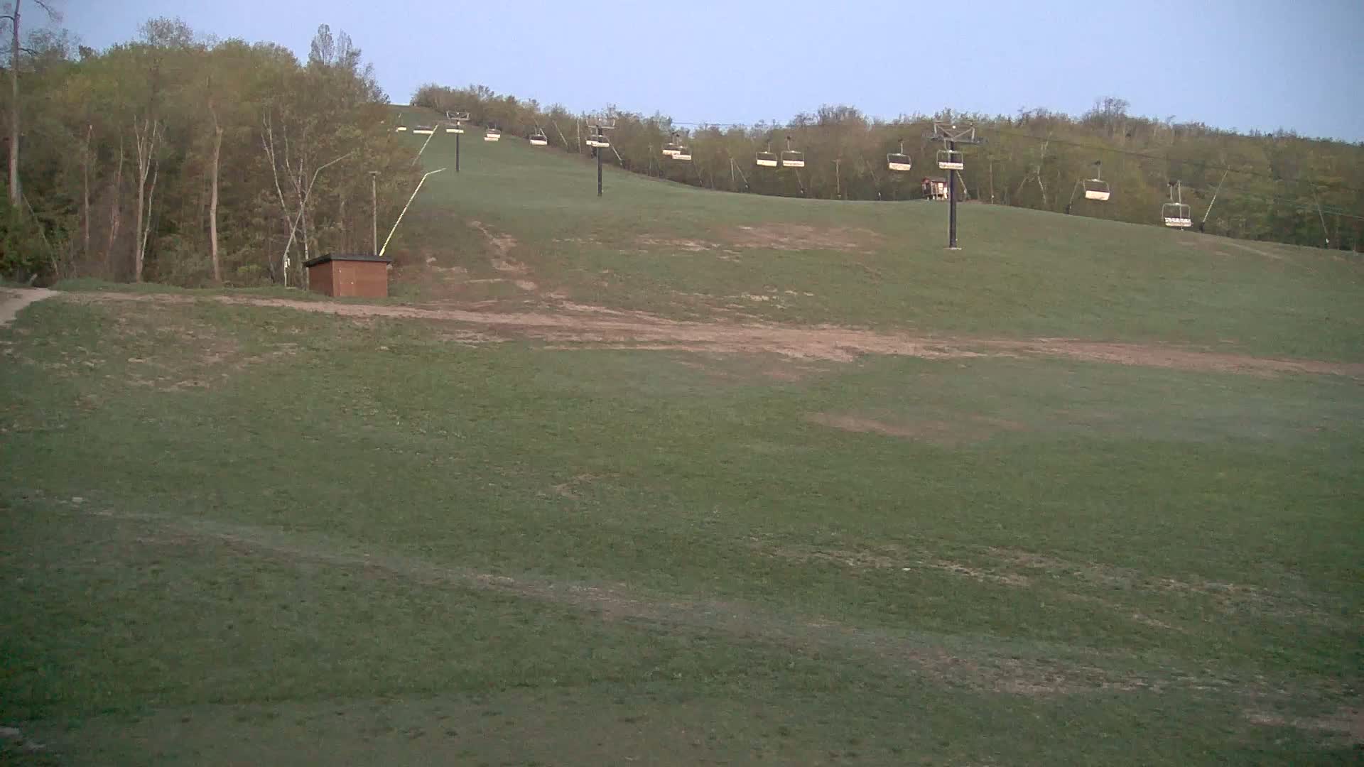 A grassy hill with a ski lift and small building is visible under a clear, dusky sky.