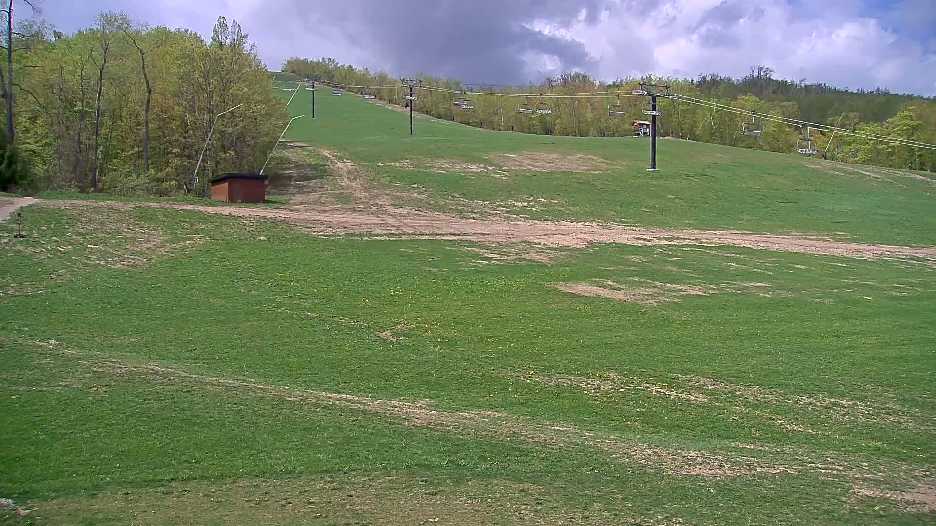 A grassy hillside with a chairlift and a small shed under partly cloudy skies.