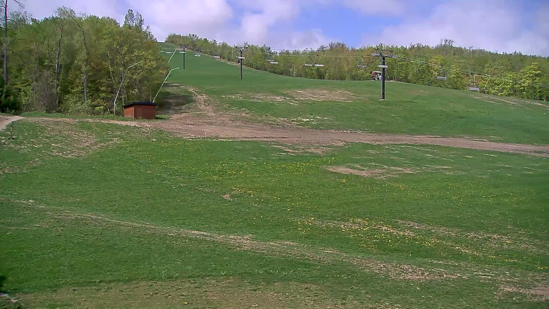A grassy hillside with a ski lift and a small brown building is visible under a mostly sunny sky.