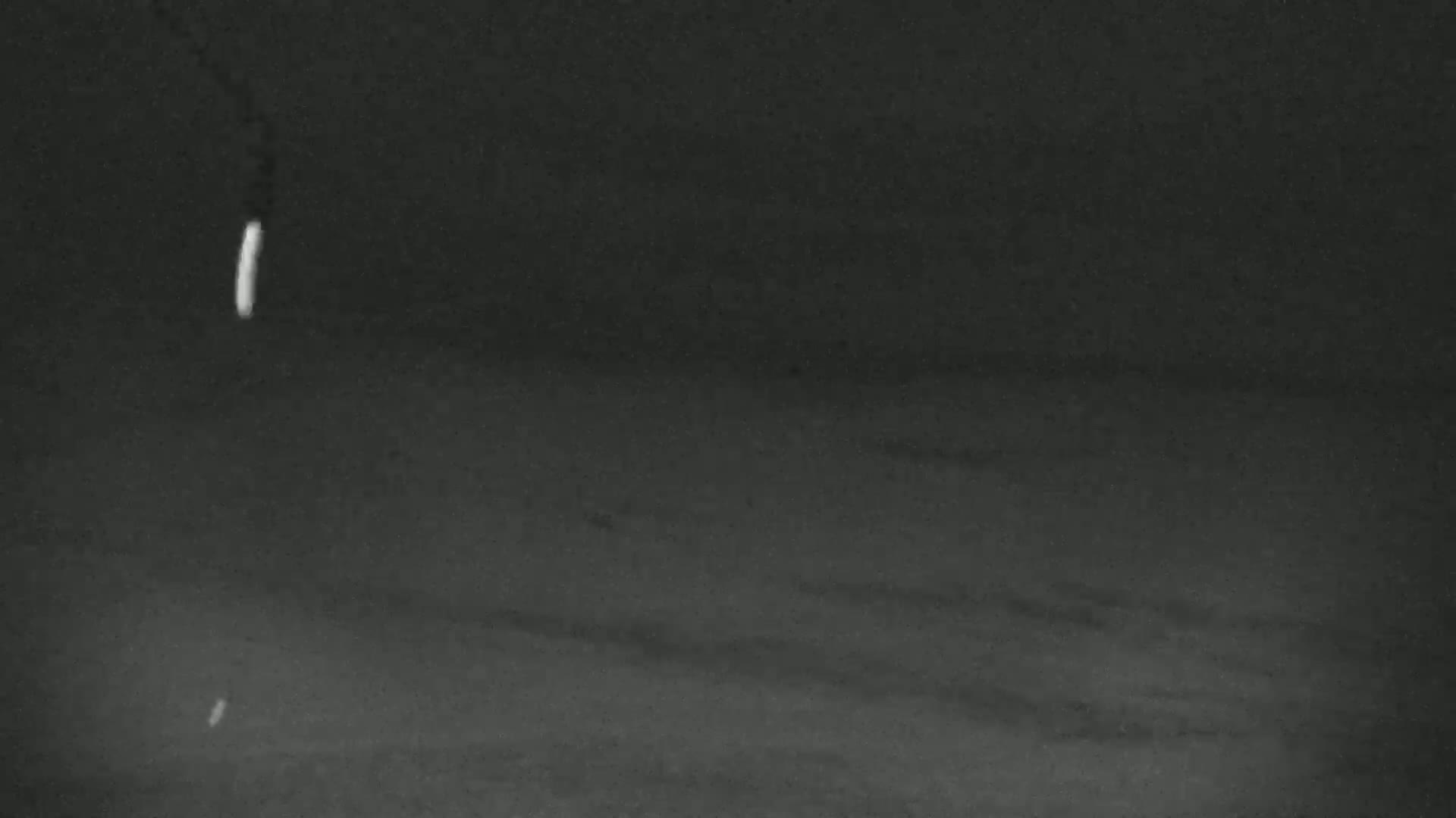 A dark, possibly nighttime, scene shows two faint, vertical streaks of light against a textured, dark gray background.