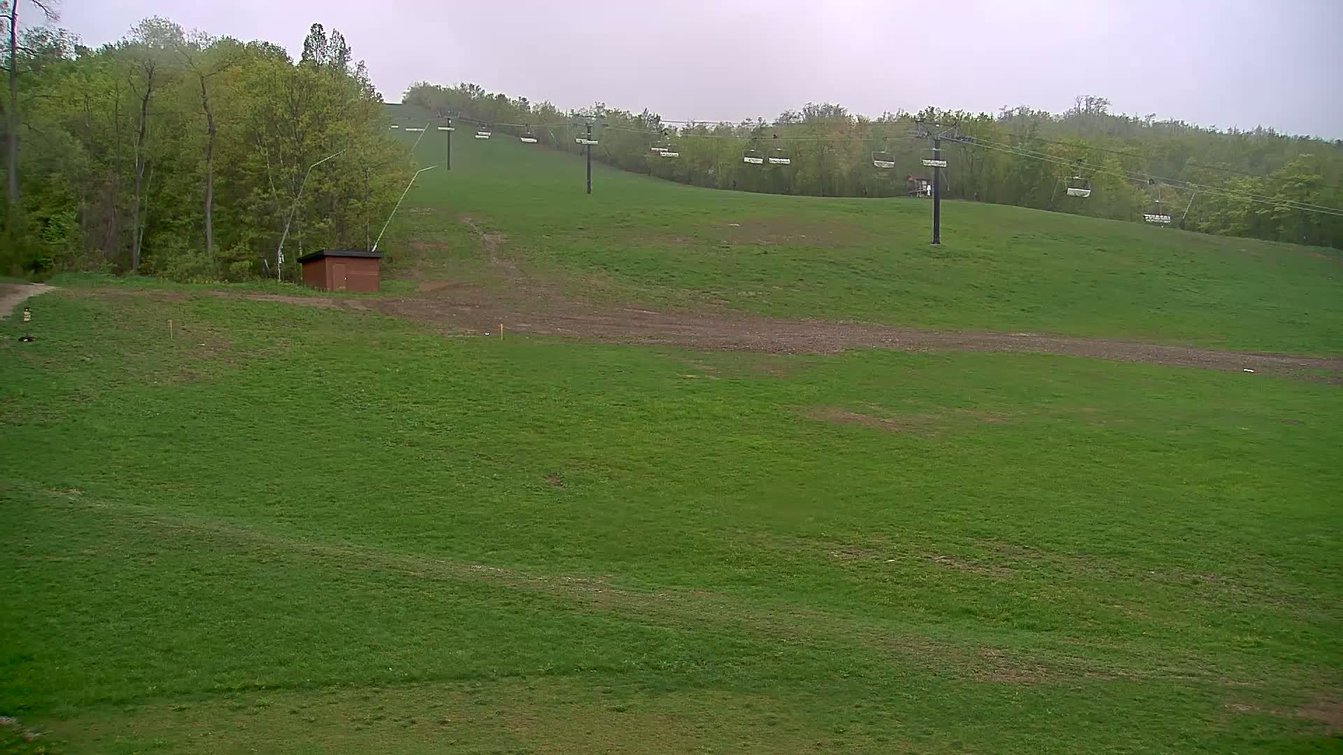 A grassy hill with a chairlift and a small brown building is visible under an overcast sky.