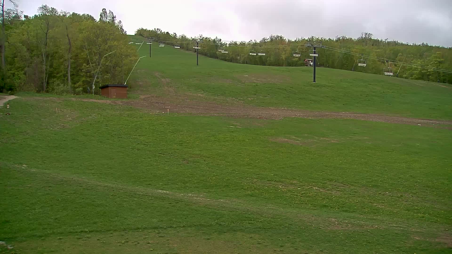 A grassy hill with a chairlift and a small brown building under an overcast sky.