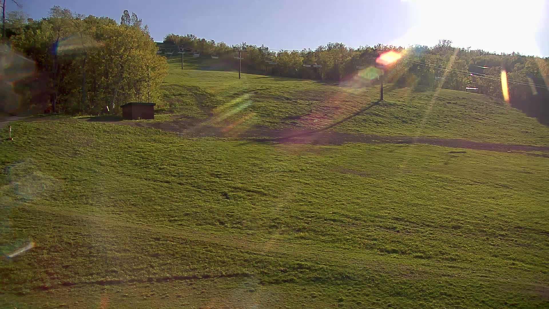 A grassy hillside with a small building and a chairlift in the background under a sunny sky.
