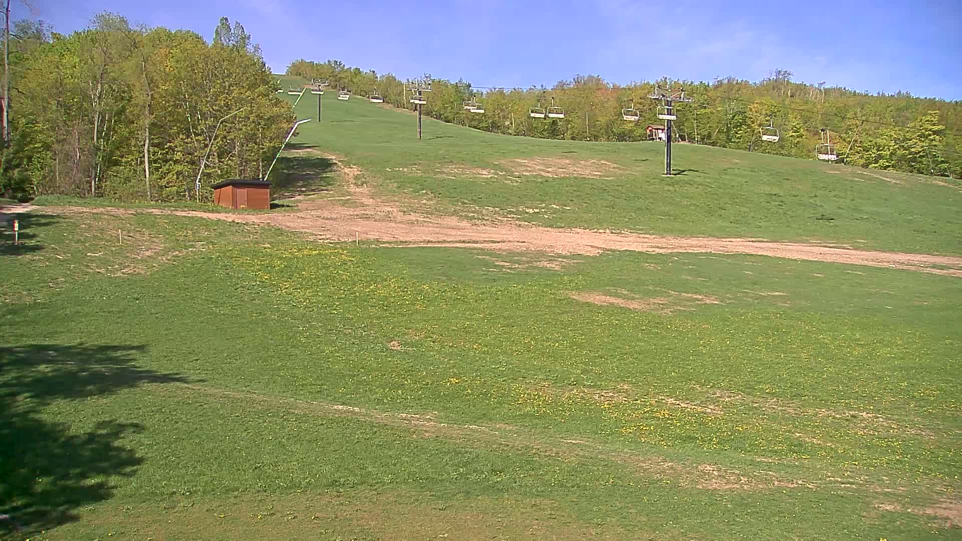 A grassy hillside with a chairlift and a small brown building, under a sunny sky.