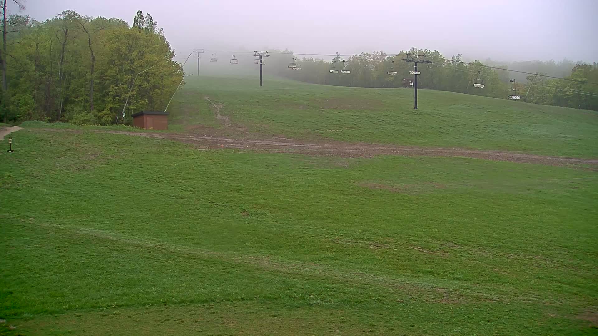 A grassy hillside with a chairlift and a small building in the foreground on a foggy day.