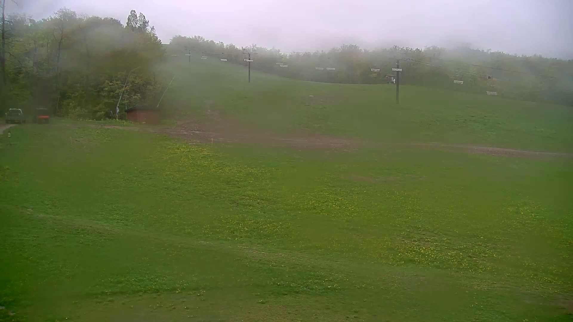 A grassy hill with a ski lift and a few small buildings is visible in the foggy, rainy weather.
