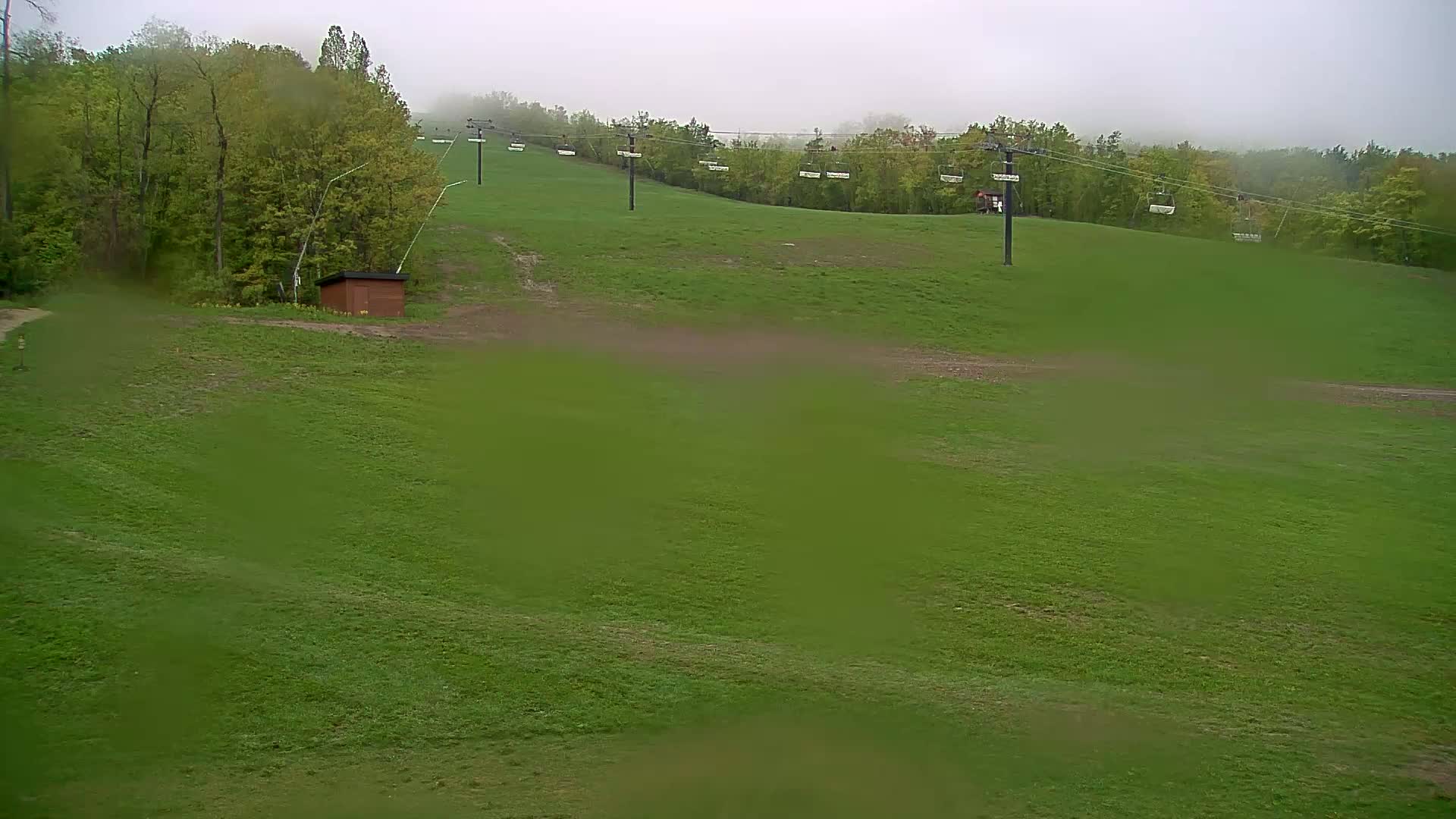 A grassy hillside with a chairlift and a small building is visible in the foggy weather.