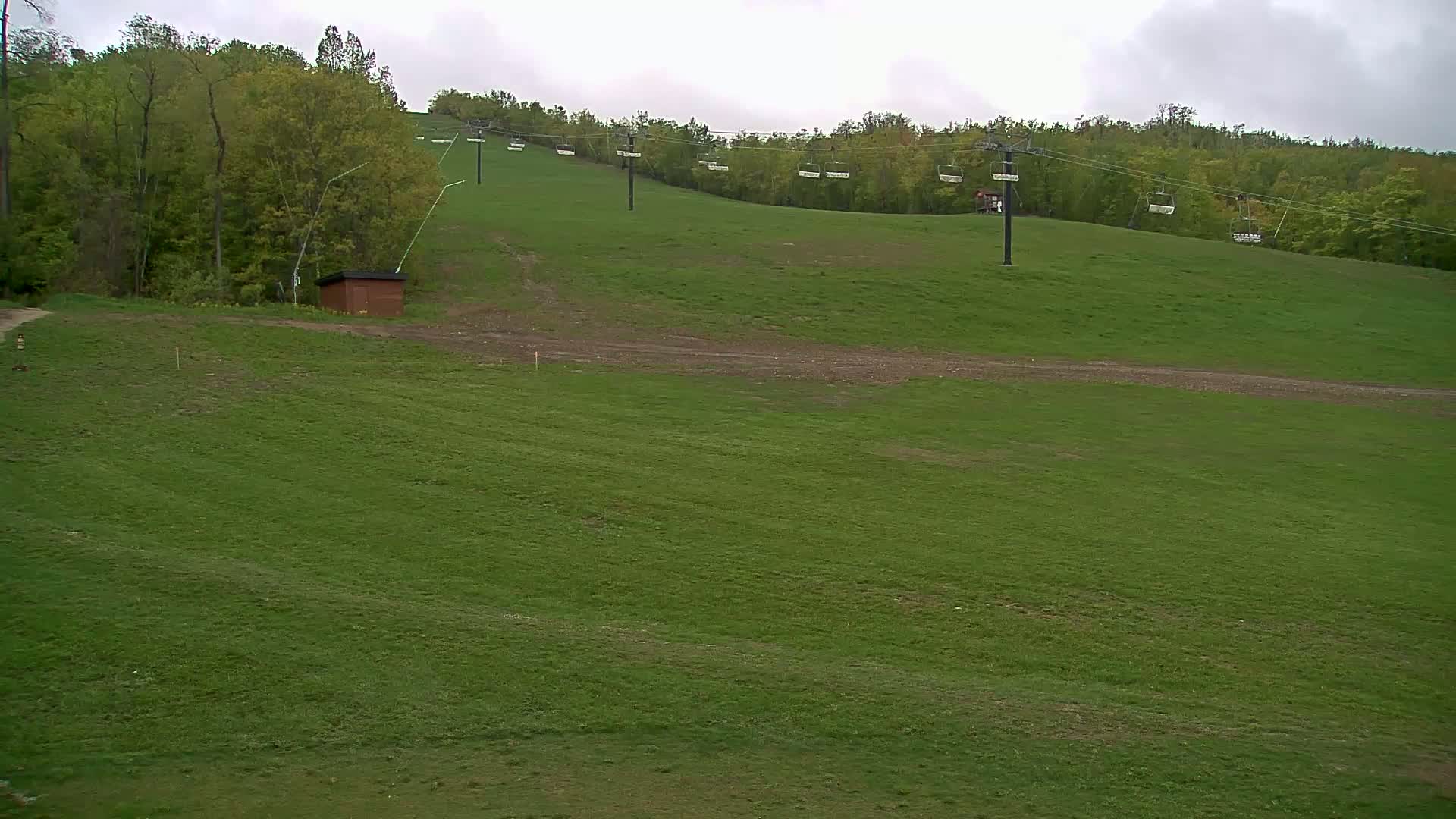 A grassy hillside with a chairlift and a small building under an overcast sky.