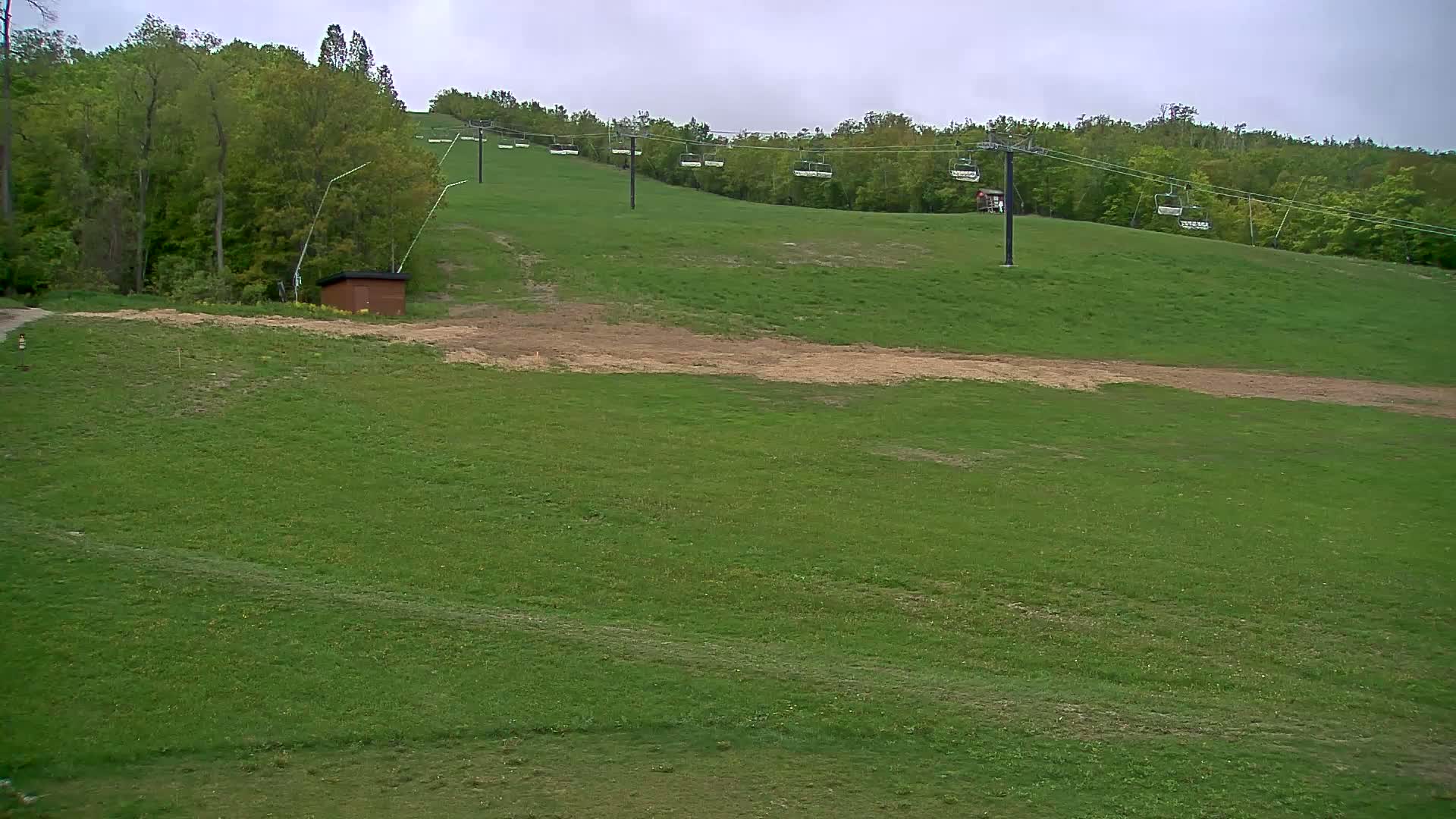 A grassy hillside with a chairlift and a small brown building, under a cloudy sky.