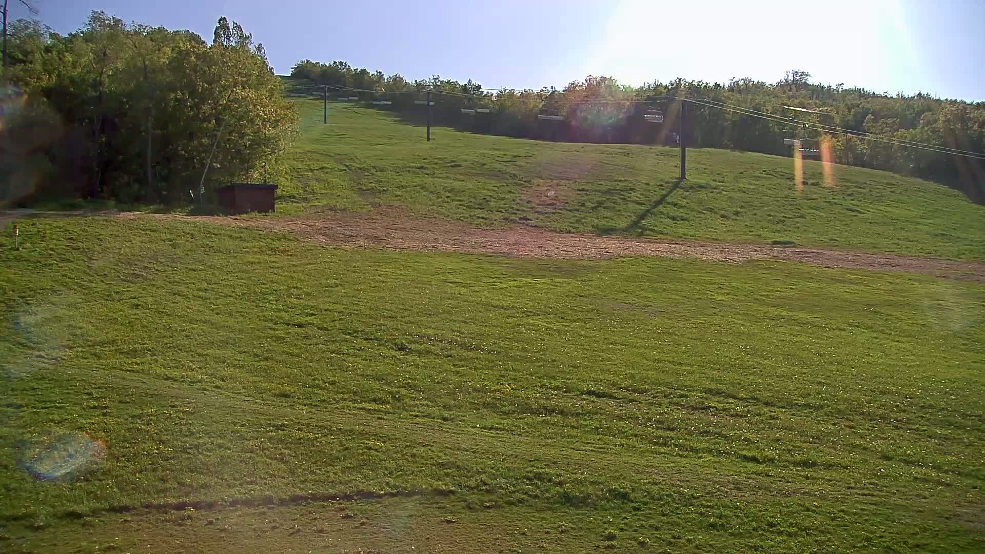 A grassy hill with a chairlift and a small shed, under sunny conditions.