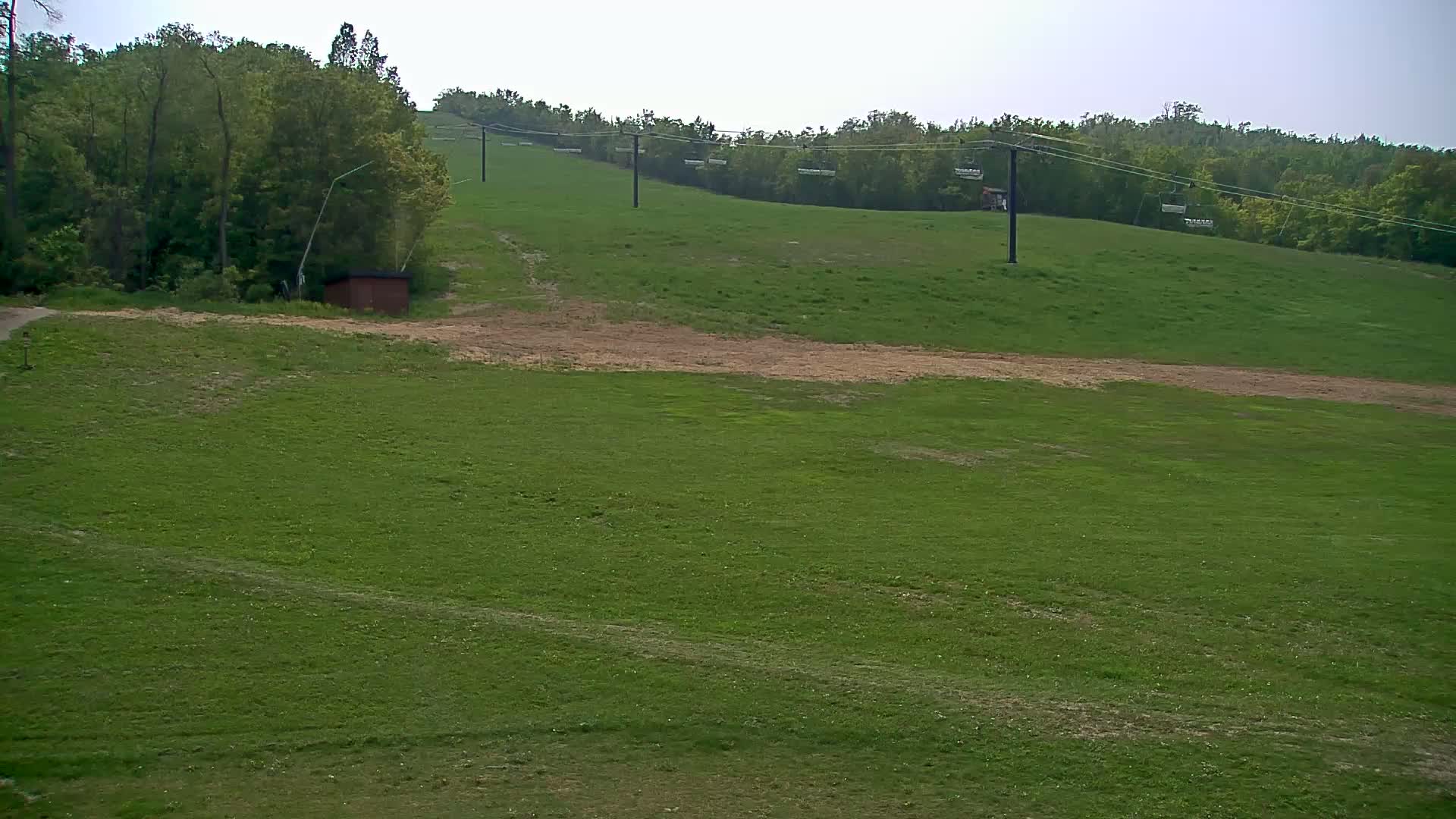 A grassy hillside with a chairlift and a small building, under a mostly clear sky.
