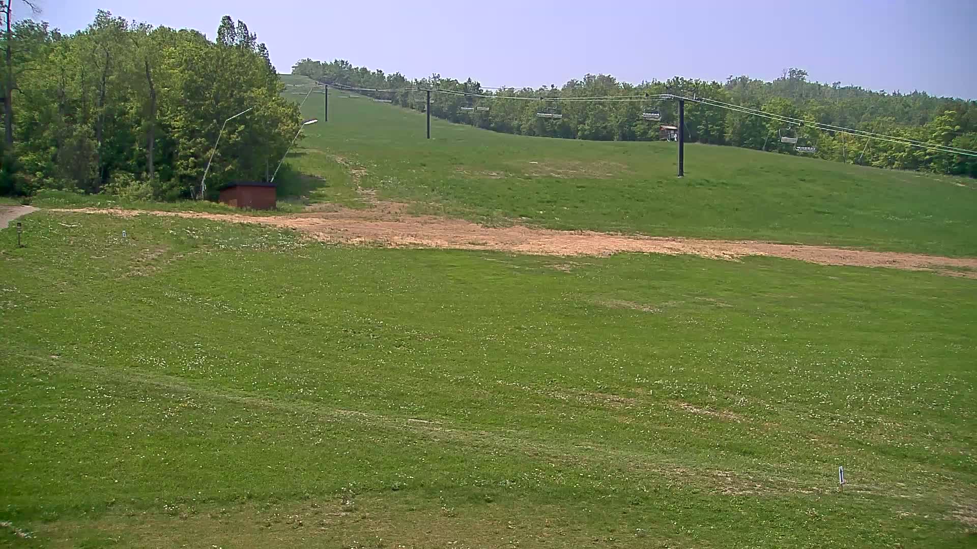 A grassy hillside with a ski lift and a small building in the foreground under a clear sky.