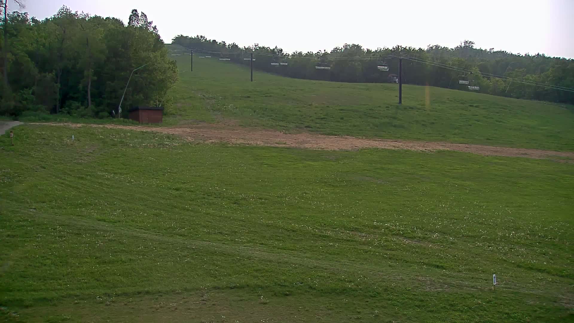 A grassy hill with a chairlift and a small brown building is visible under an overcast sky.