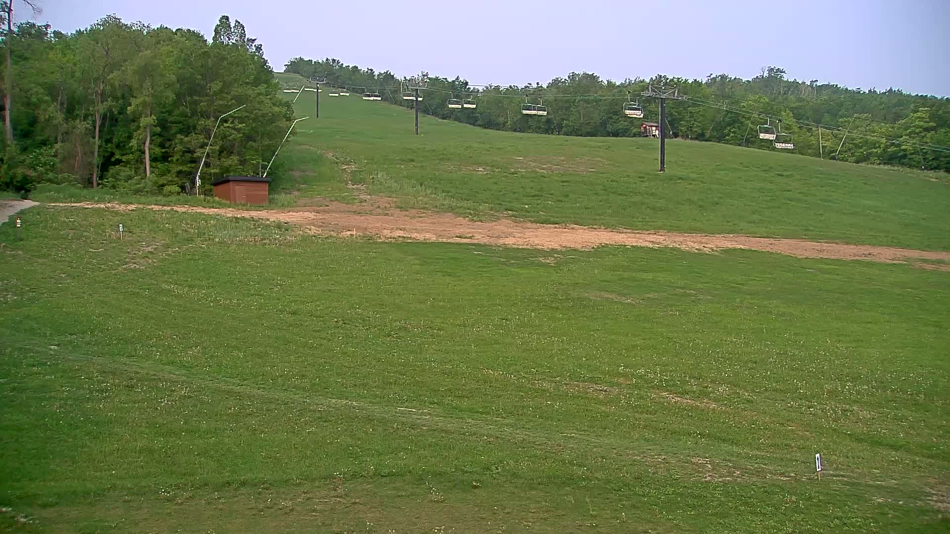 A grassy hillside with a chairlift and a small brown building under an overcast sky.