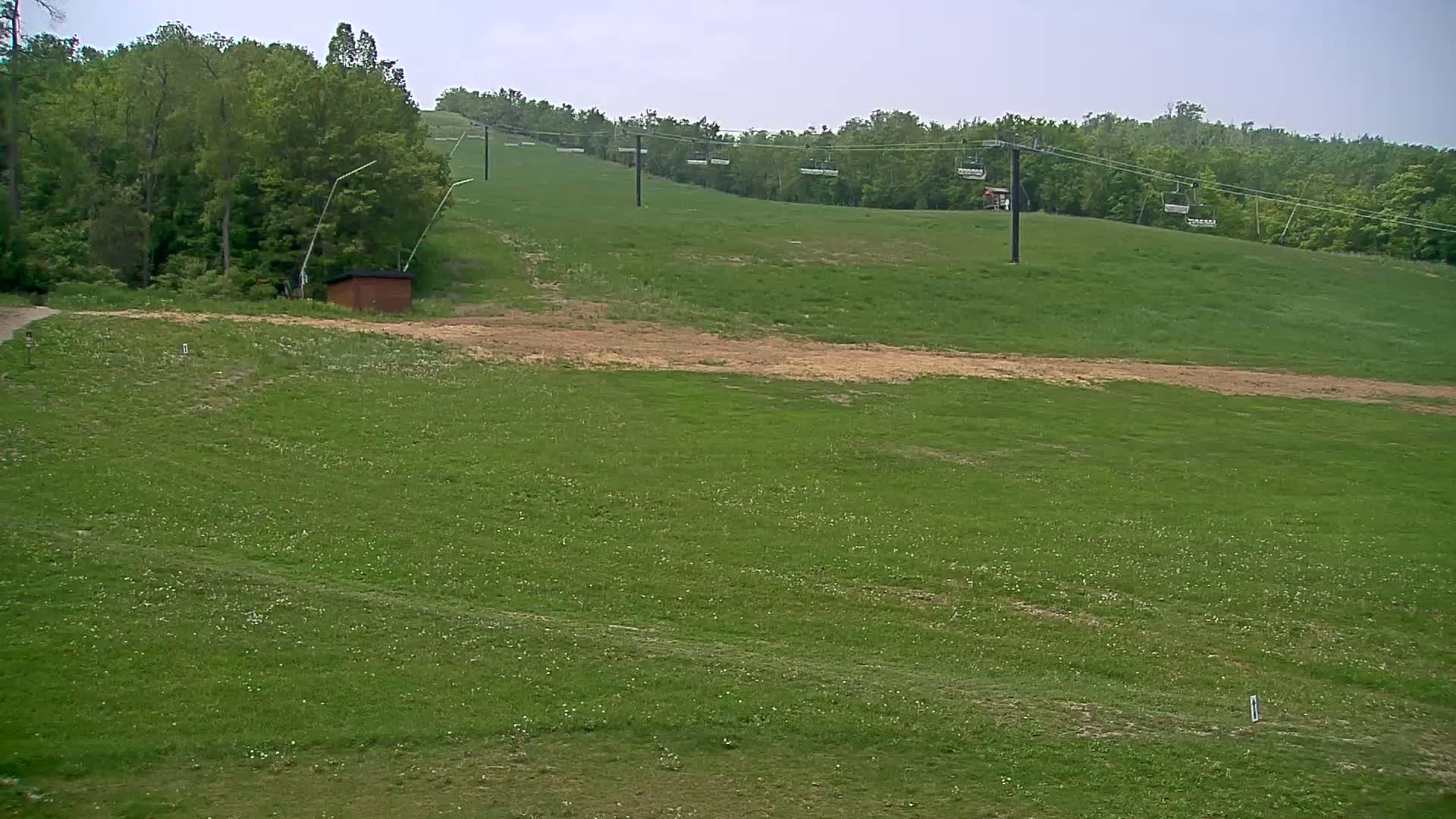 A grassy hillside with a chairlift and a small brown building is visible under an overcast sky.