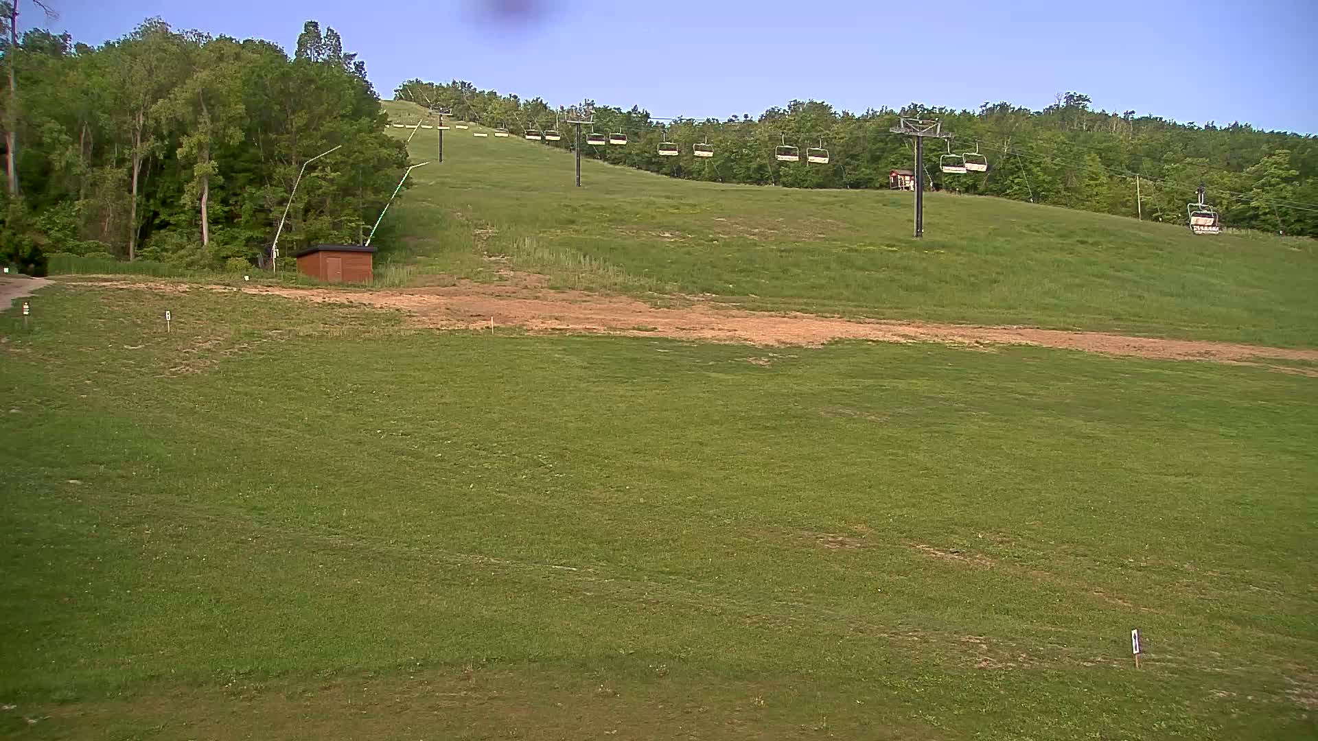 A grassy hill with a chairlift and a small building under a clear blue sky.