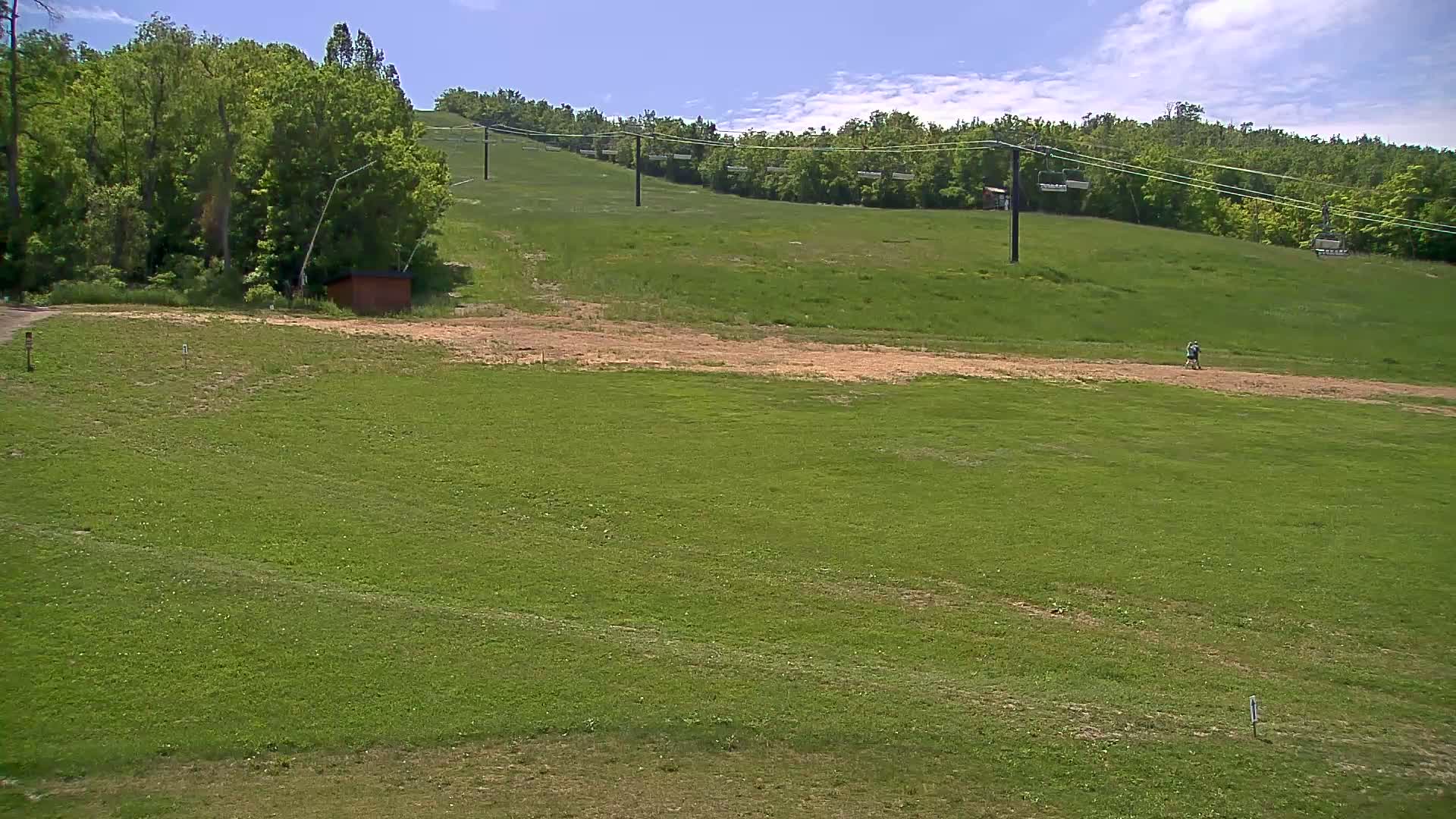 A grassy hill with a ski lift and a small building in the foreground under a partly cloudy sky.