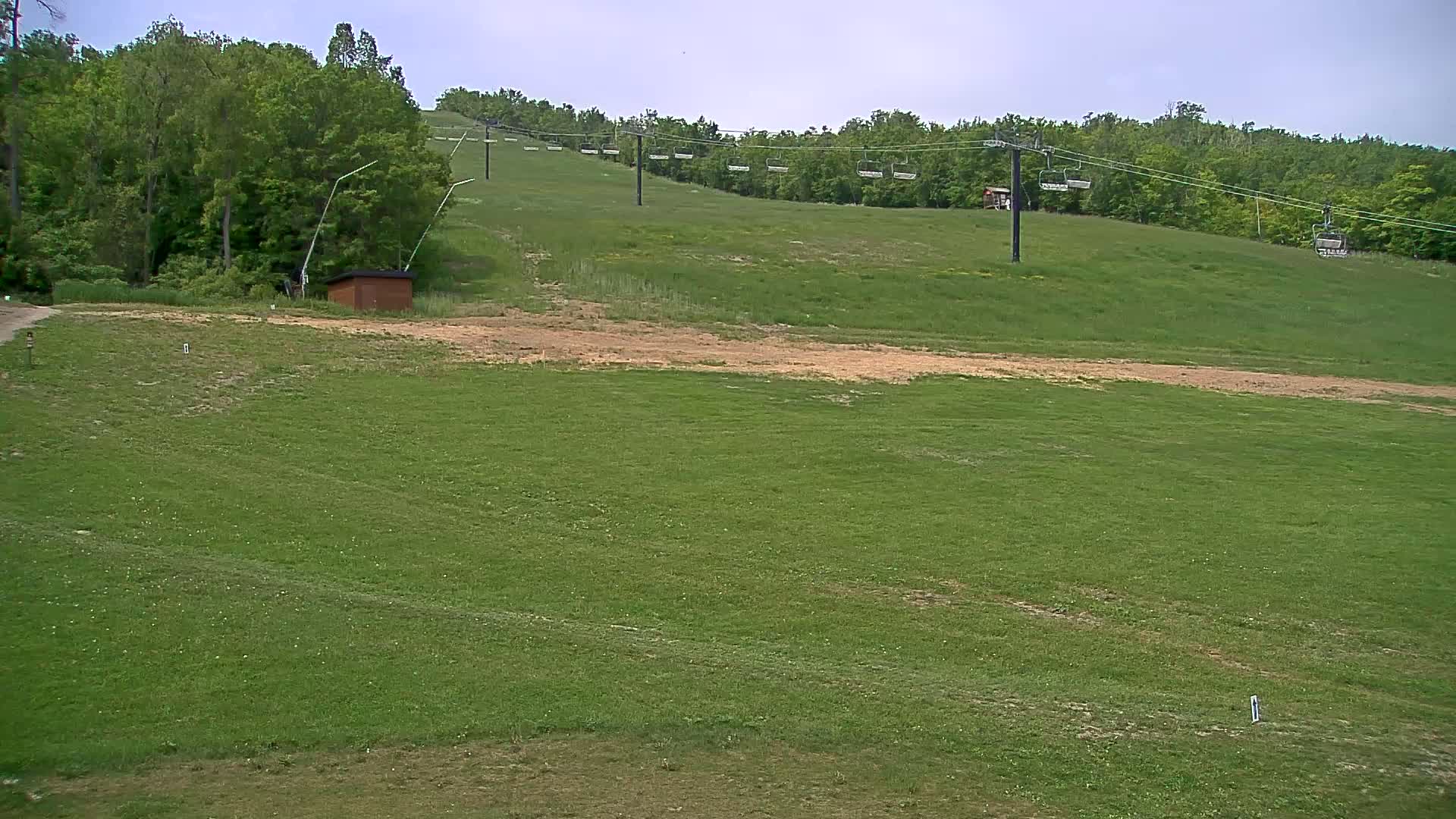 A grassy hillside with a chairlift and a small brown building, under a mostly cloudy sky.