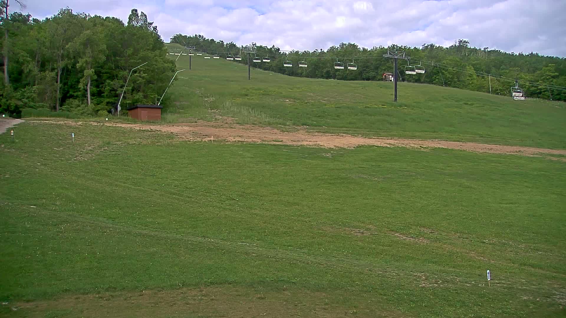 A grassy hillside with a chairlift and a small building under partly cloudy skies.