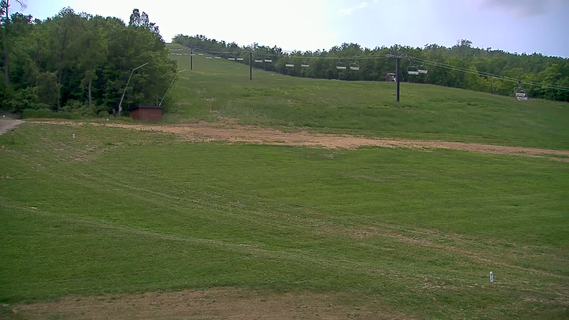 A grassy field with a chairlift extending up a hillside under a partly cloudy sky.
