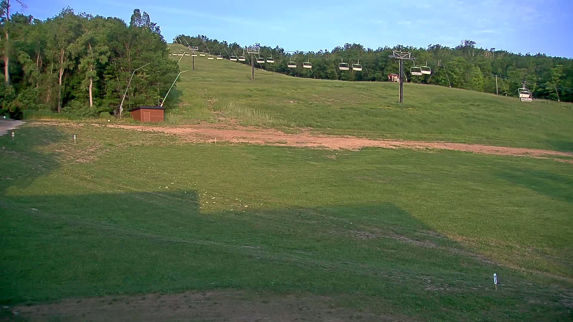 A grassy hillside with a chairlift and a small brown building is visible under a clear sky.