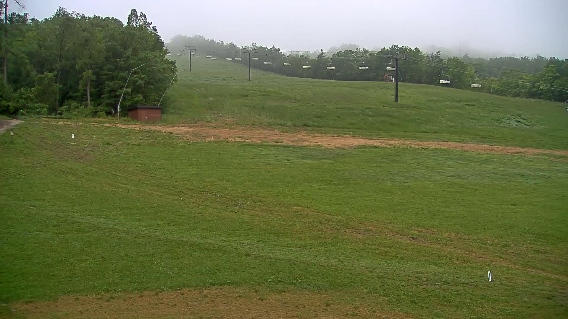 A grassy hill with a chairlift running across it is visible in the foggy weather.