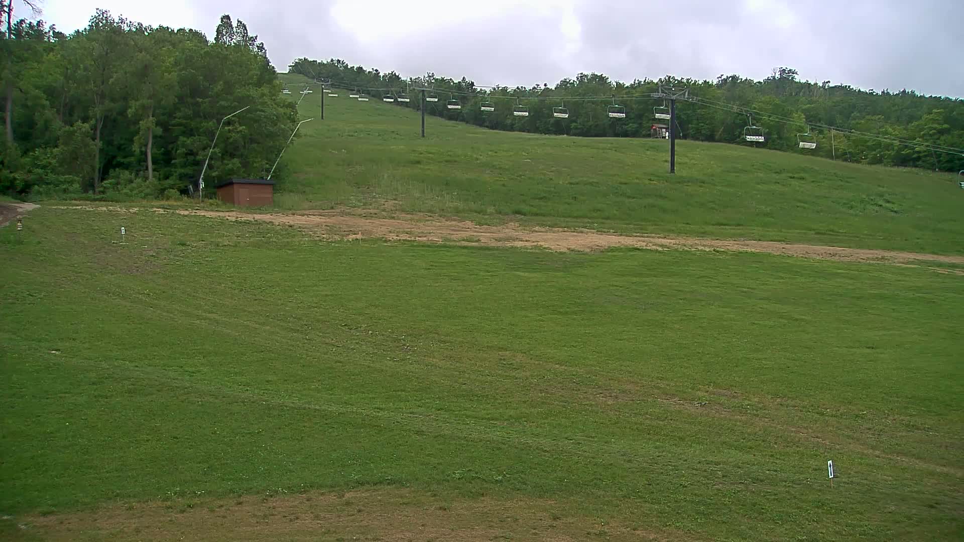 A grassy hillside with an empty chairlift in the background under an overcast sky.