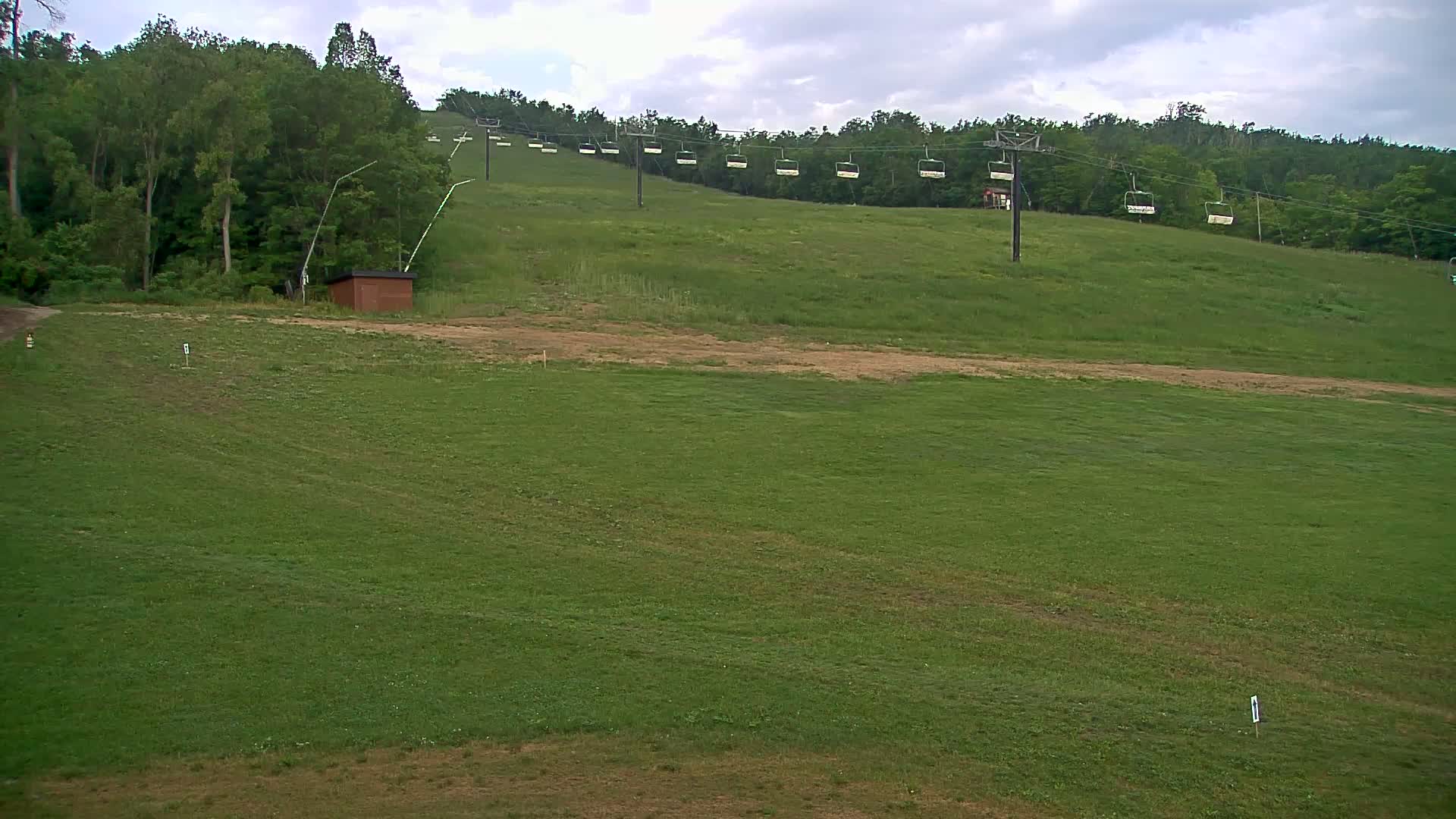 A grassy hillside with a chairlift and a small building under a partly cloudy sky.