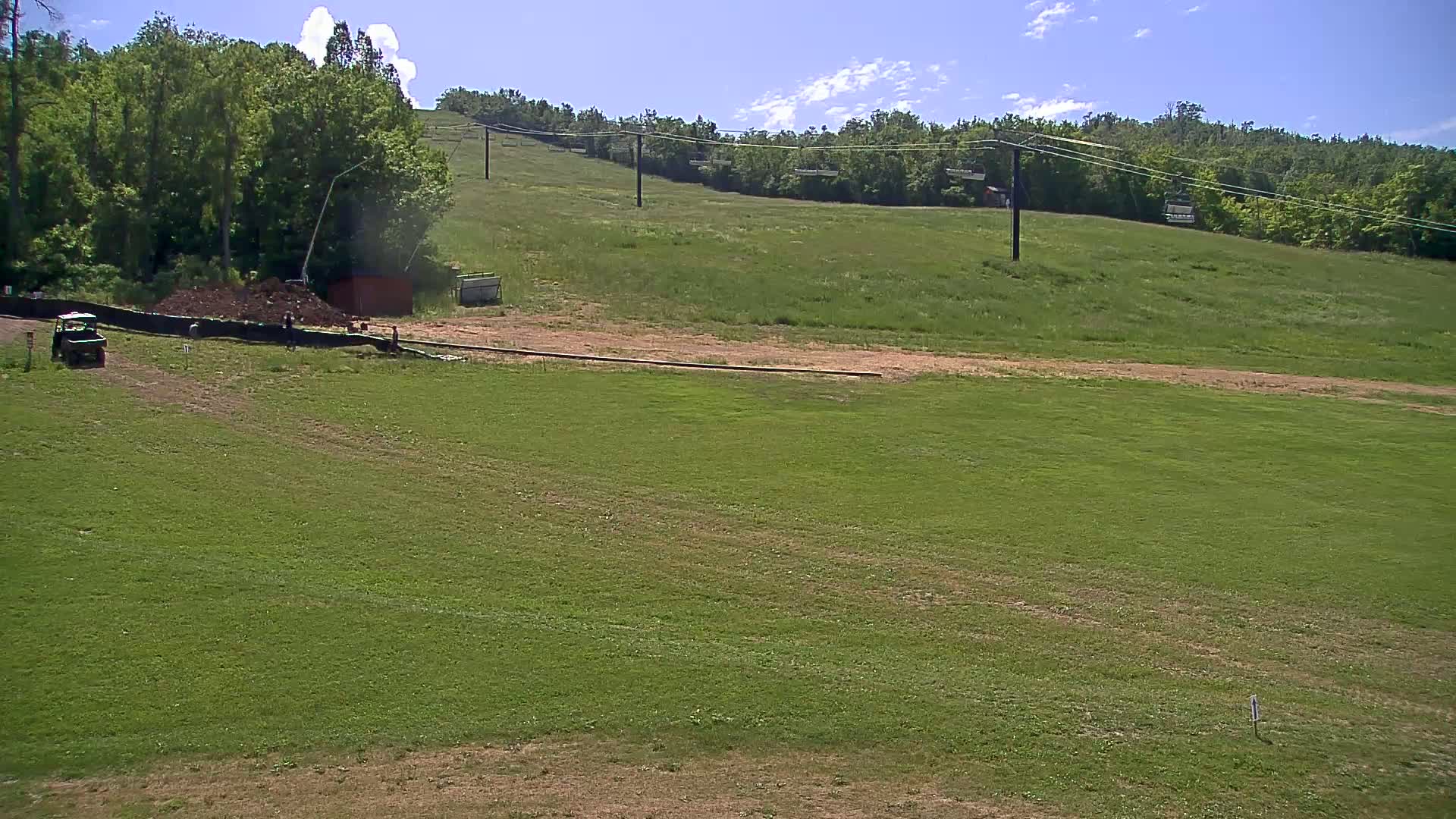 A grassy field with a chairlift in the background under a partly cloudy sky.