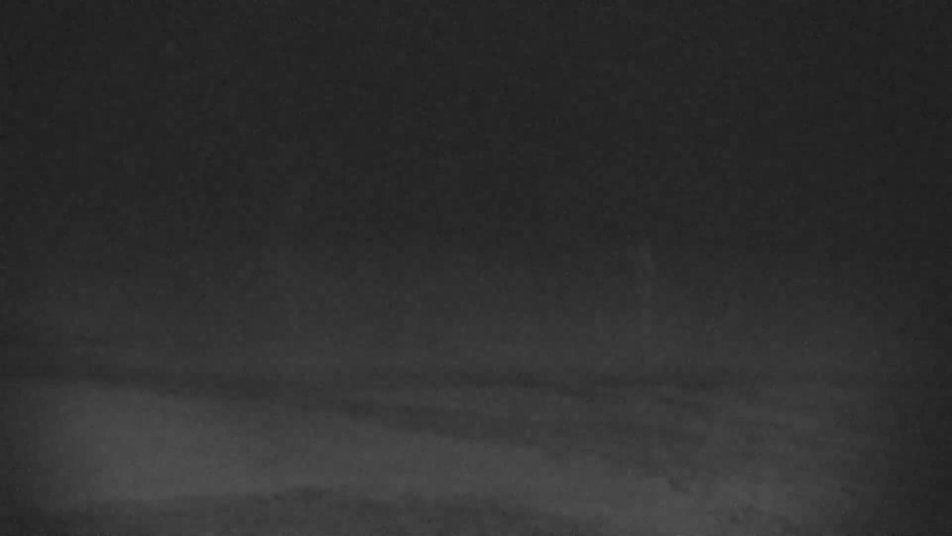 A very dark, low-light image of an outdoor night scene reveals an indistinct horizon separating a faint, textured foreground from an opaque sky, suggesting extremely poor visibility due to fog or heavy cloud cover.