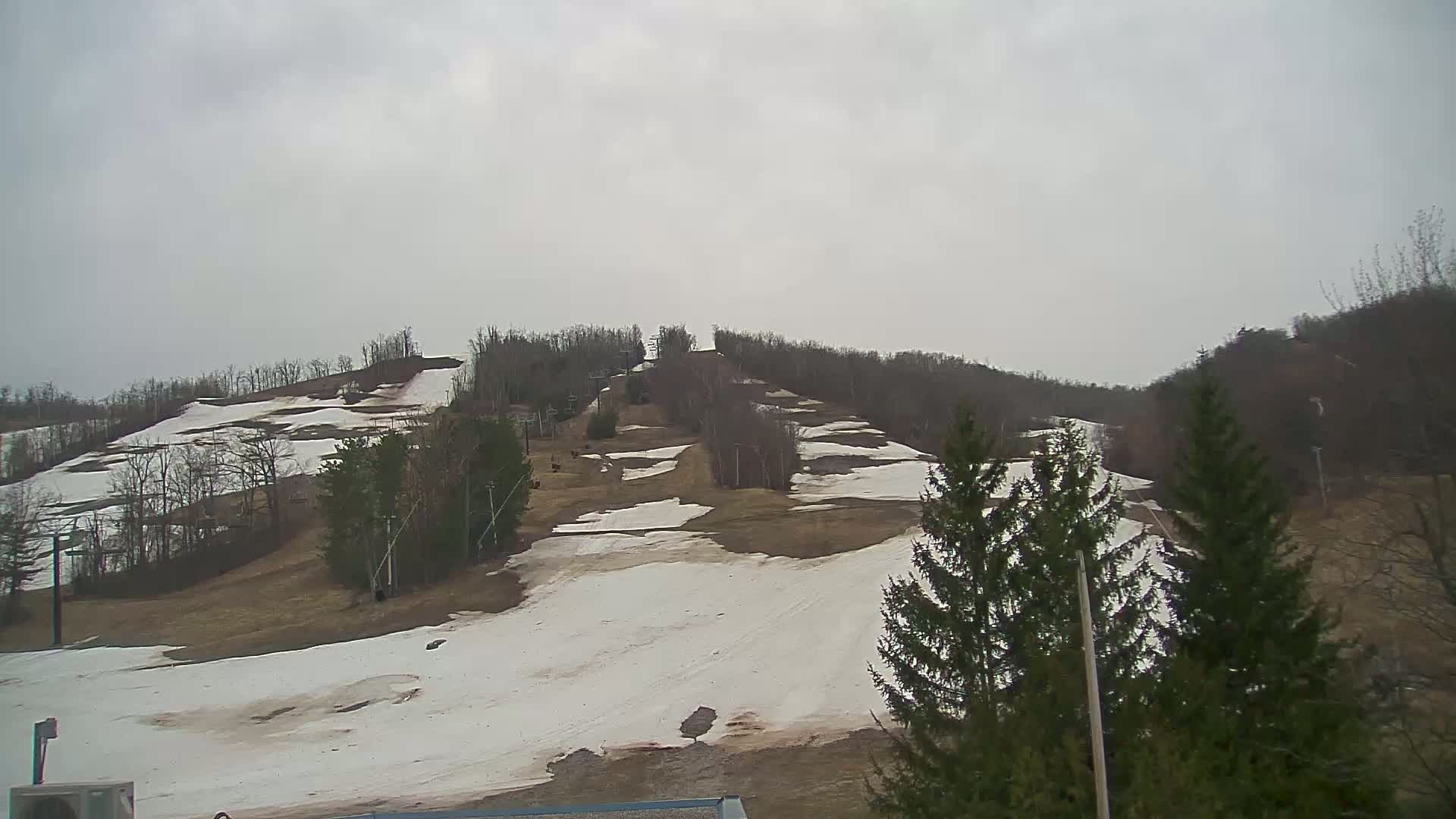 A ski slope with patches of melting snow is visible under an overcast sky.